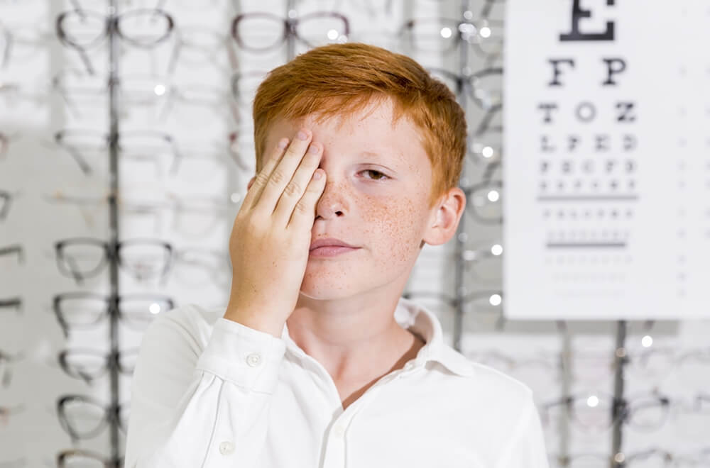 cute-boy-covered-his-eye-with-hand-standing-optics-clinic.jpg