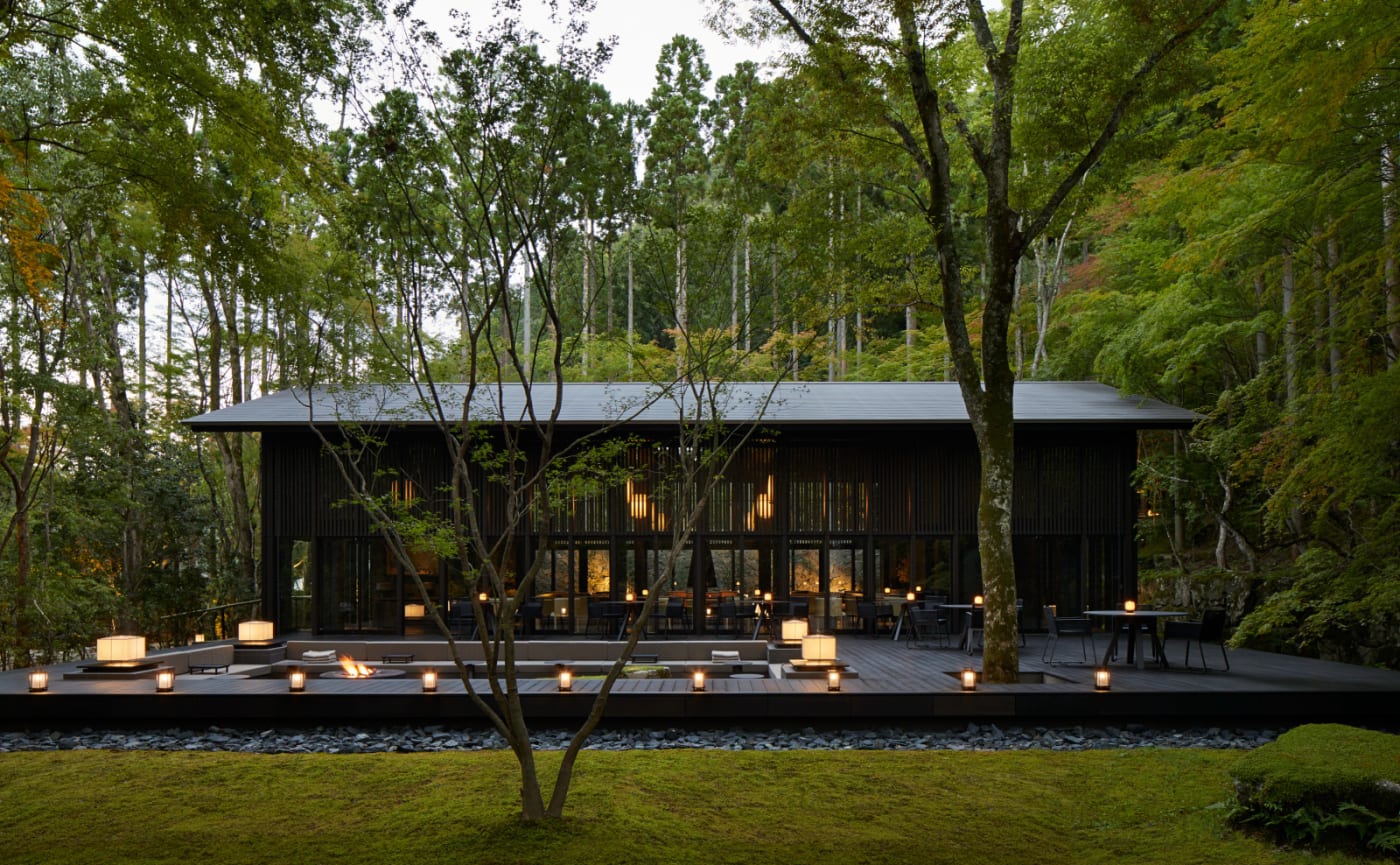 Un pavillon de l'Aman Kyoto dans la forêt, éclairé de lanternes au crépuscule