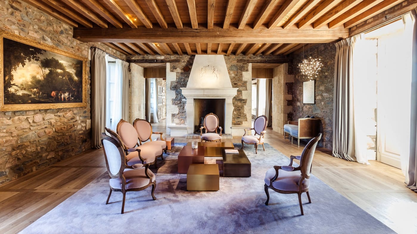Sitting room in the château at the Domaine des Étangs, with beams, stone walls, a fireplace and antique armchairs