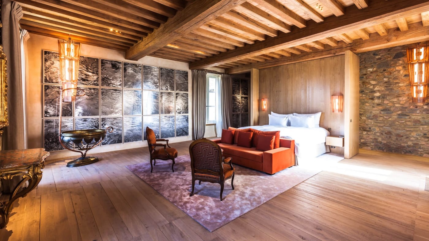 Bedroom in the château at the Domaine des Étangs beneath the beams, with artworks and an orange sofa