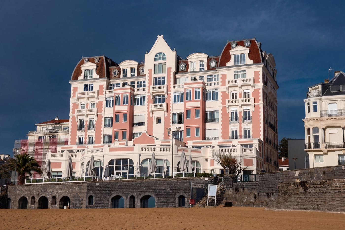 The pink and white façade of the Grand Hôtel Spa & Thalasso in Saint-Jean-de-Luz above the beach, under a stormy sky