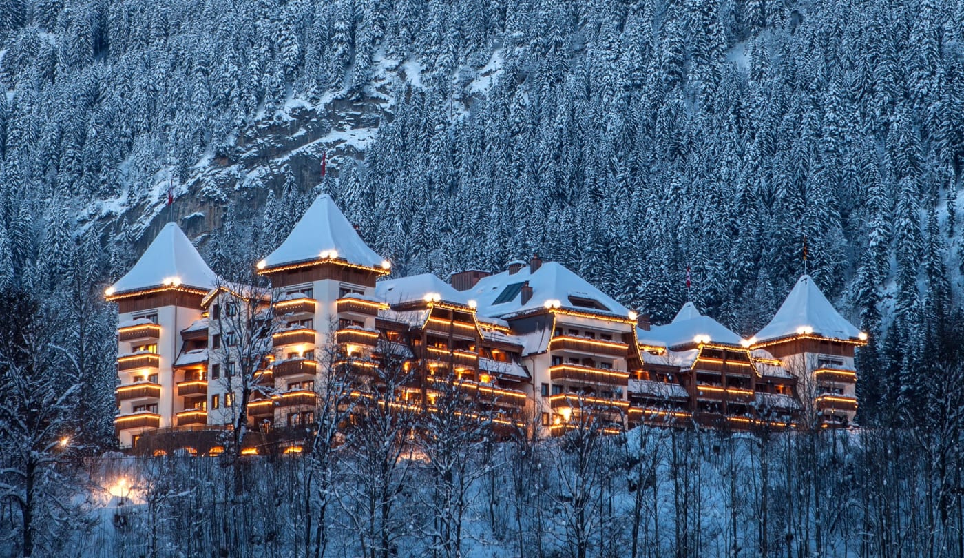 Façade illuminée de l'hôtel The Alpina Gstaad sous la neige à la tombée de la nuit