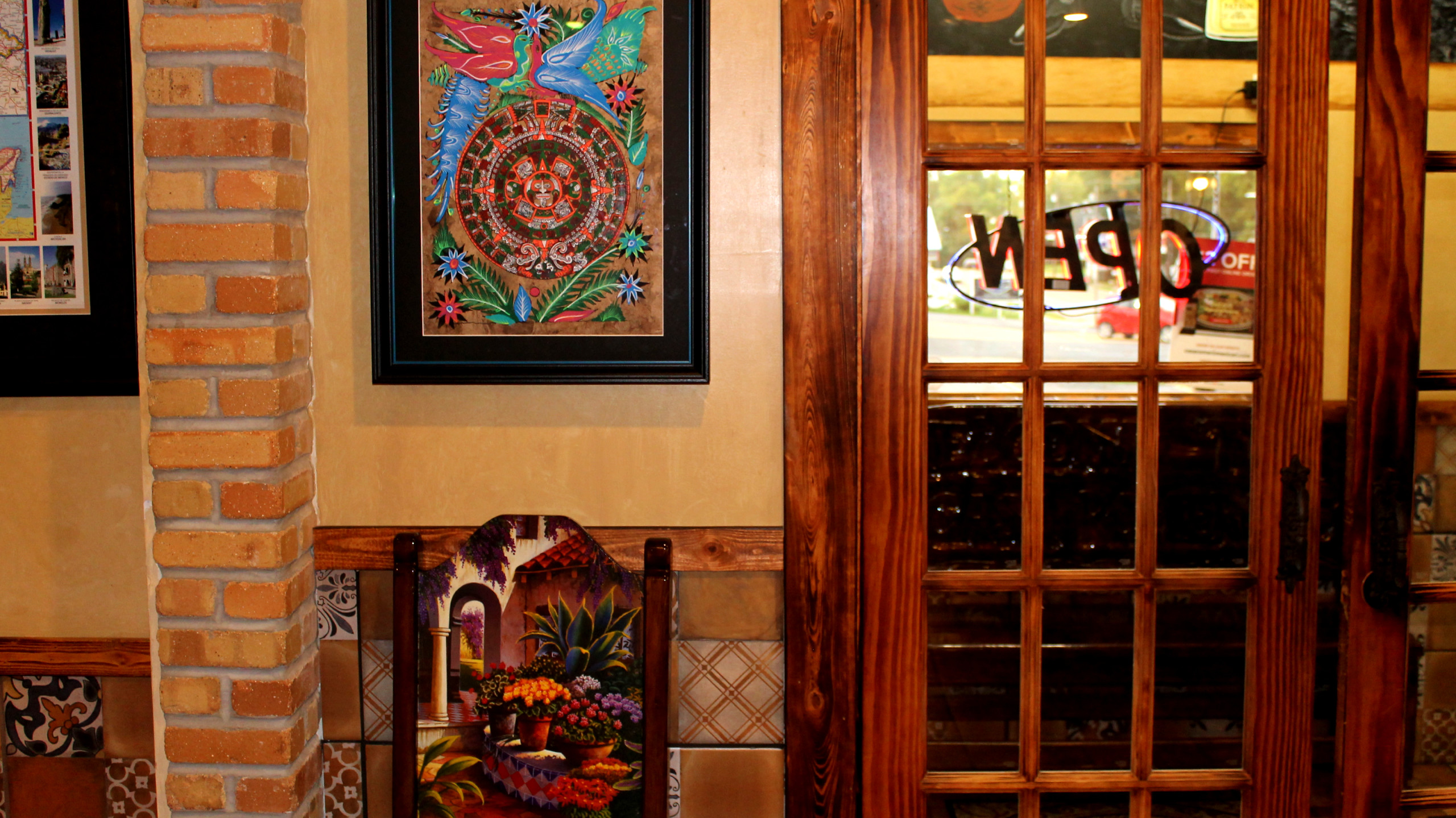 Small Mexican artwork framed and another on chair back next to a 'gridded' wood and glass door.