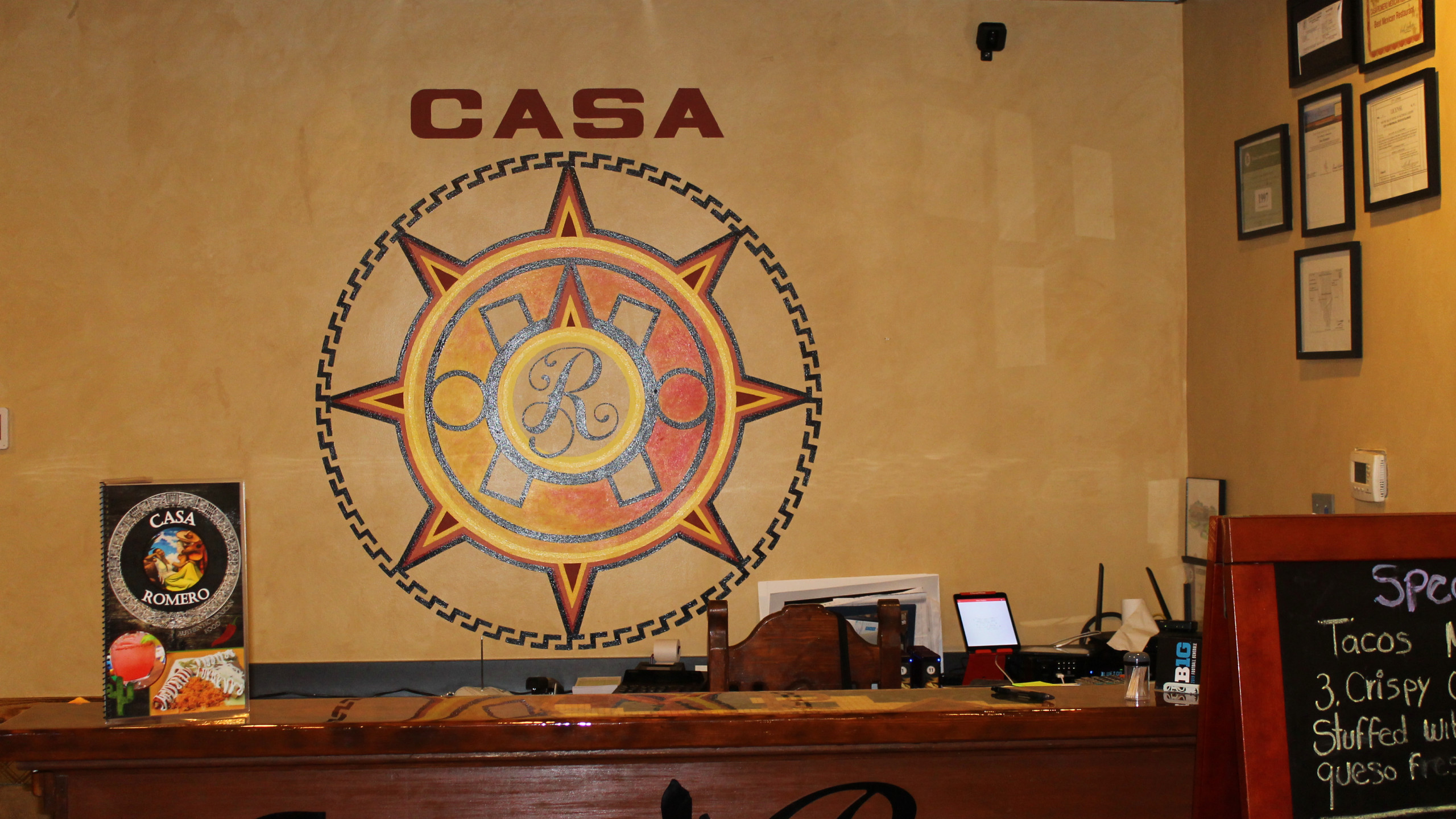 Front counter of Casa Romero showing a bright orangish-yellow design featuring a script R with 'CASA' above it.