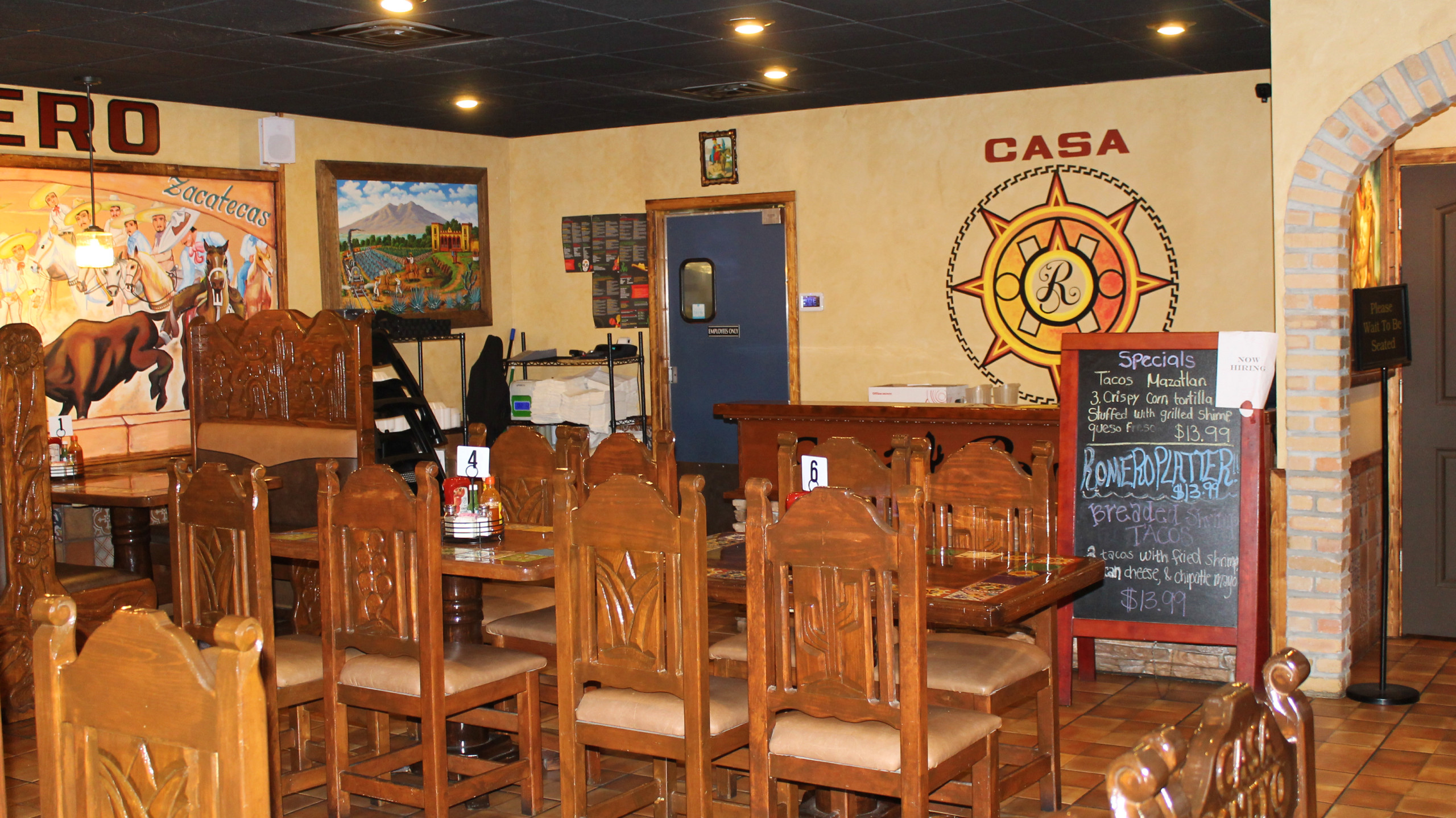 Wooden chairs with carvings, table and paintings inside restaurant.