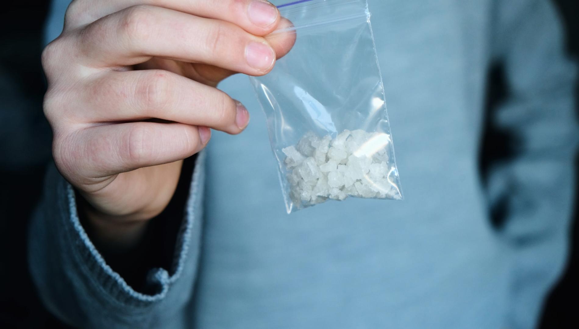 A hand holding a small plastic bag containing methamphetamine crystals