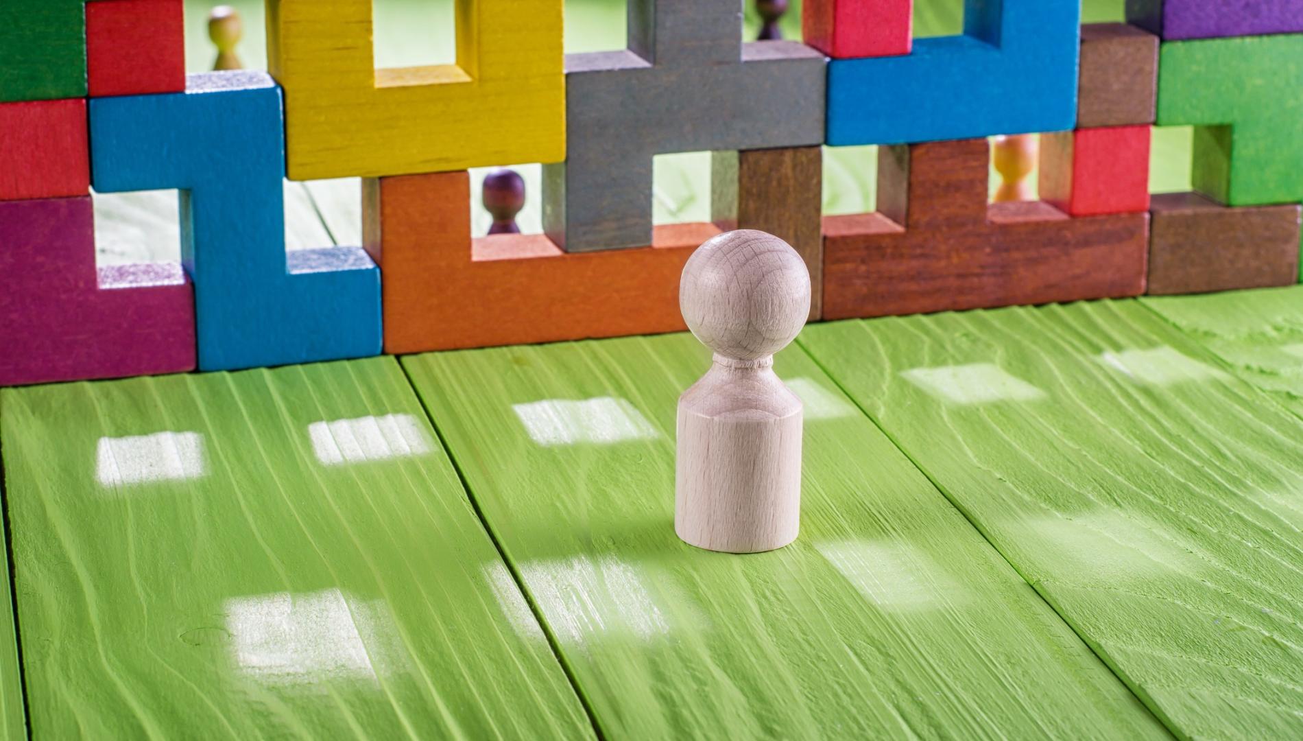 Wooden figure stands in front of a clourful barrier.