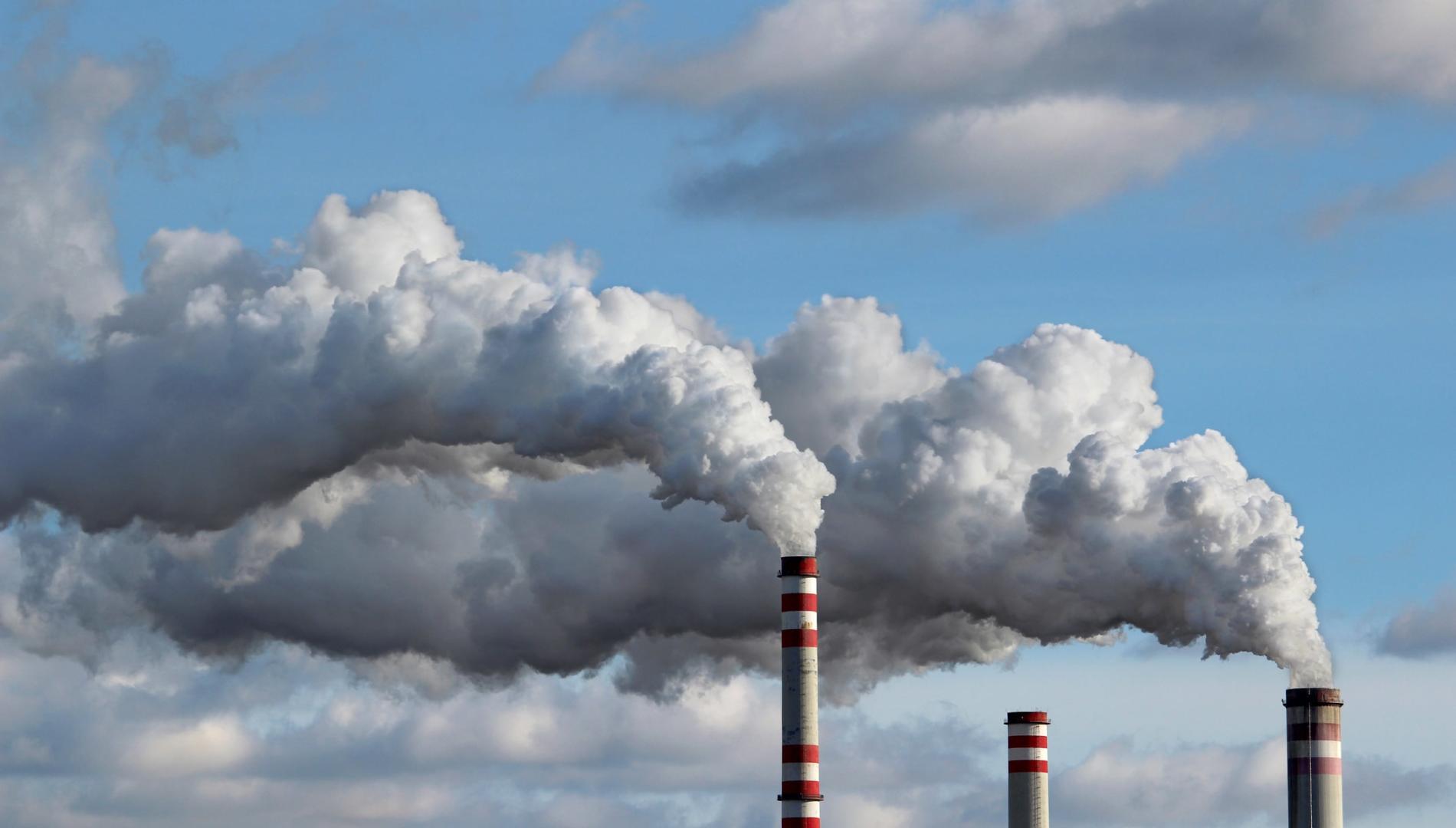 Factory chimneys emitting white smoke with blue sky in the background 