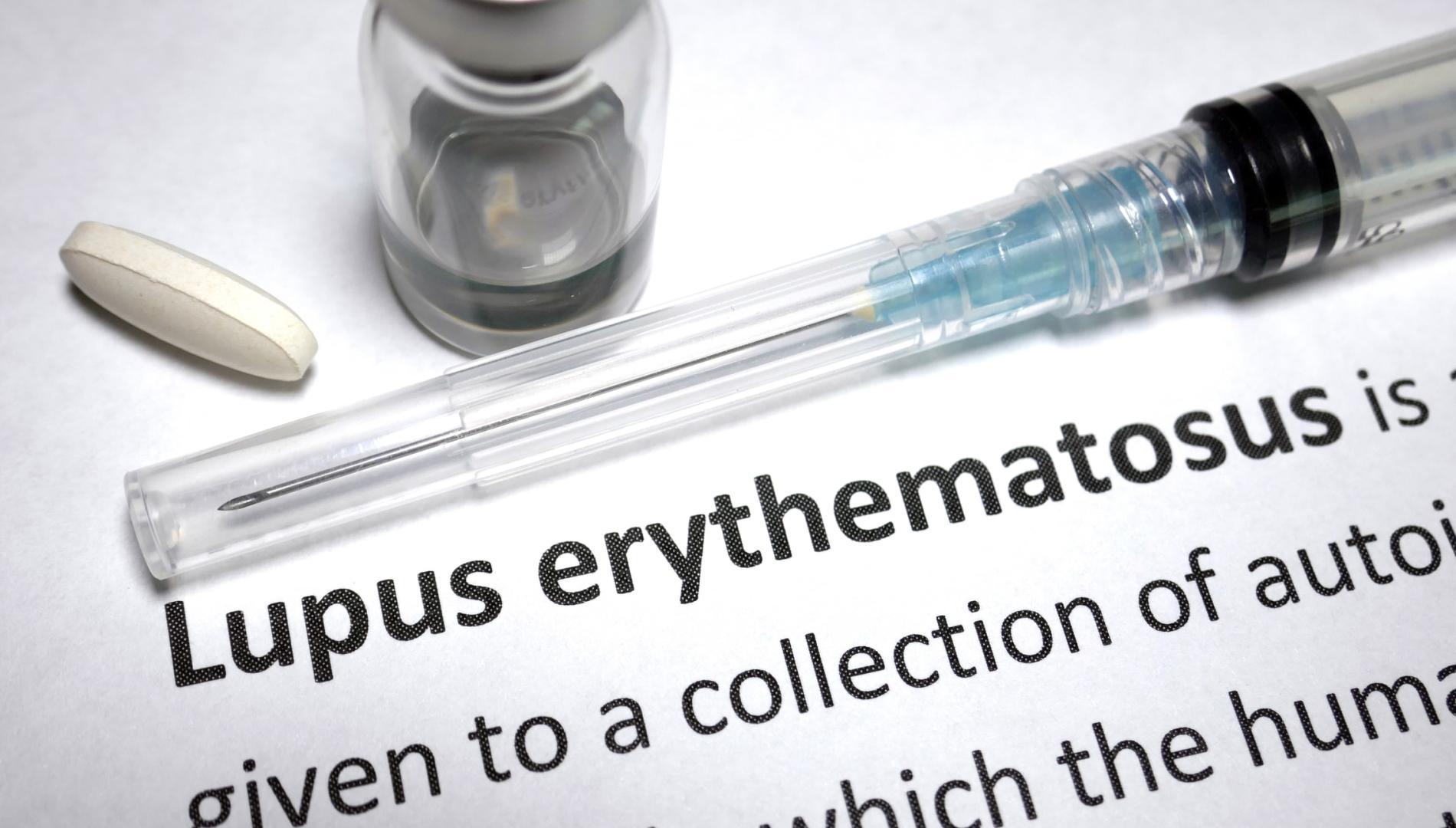 A syringe, bottle and pill sitting on writing describing Lupus erythematous