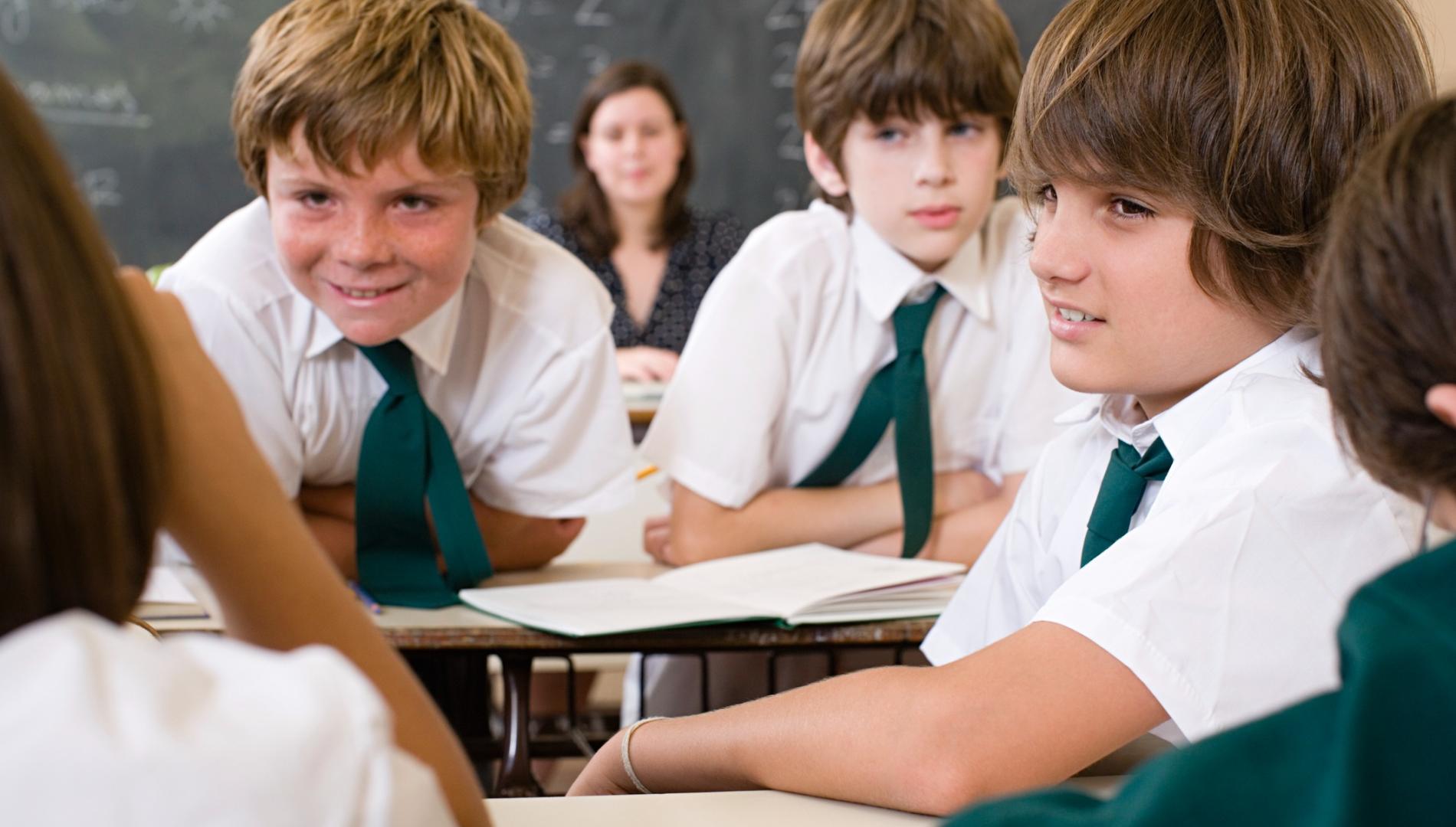 Young students in a classroom with their back to the teacher, talking during class.