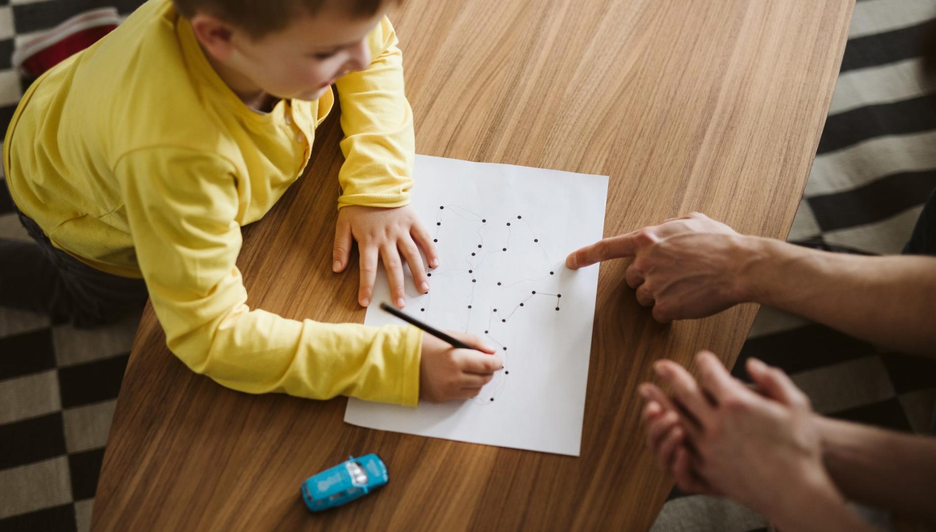 Boy kneeling on the floor and connecting dots on a piece of paper 