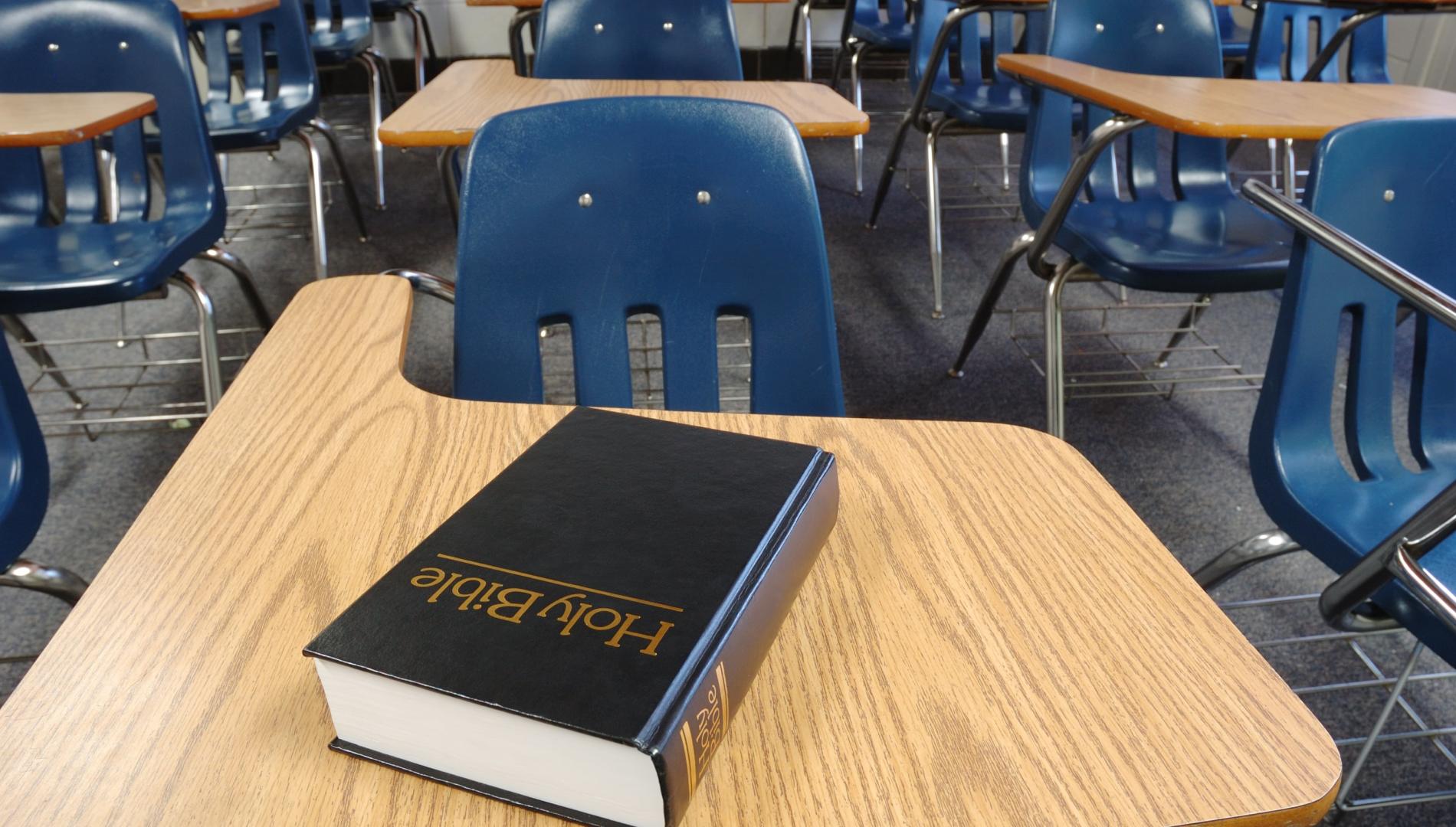 A copy of The Holy Bible on a desk in an empty classroom