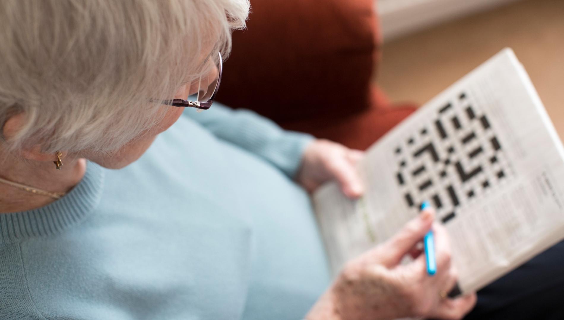 Elderly woman sitting down doing a crossword puzzle.