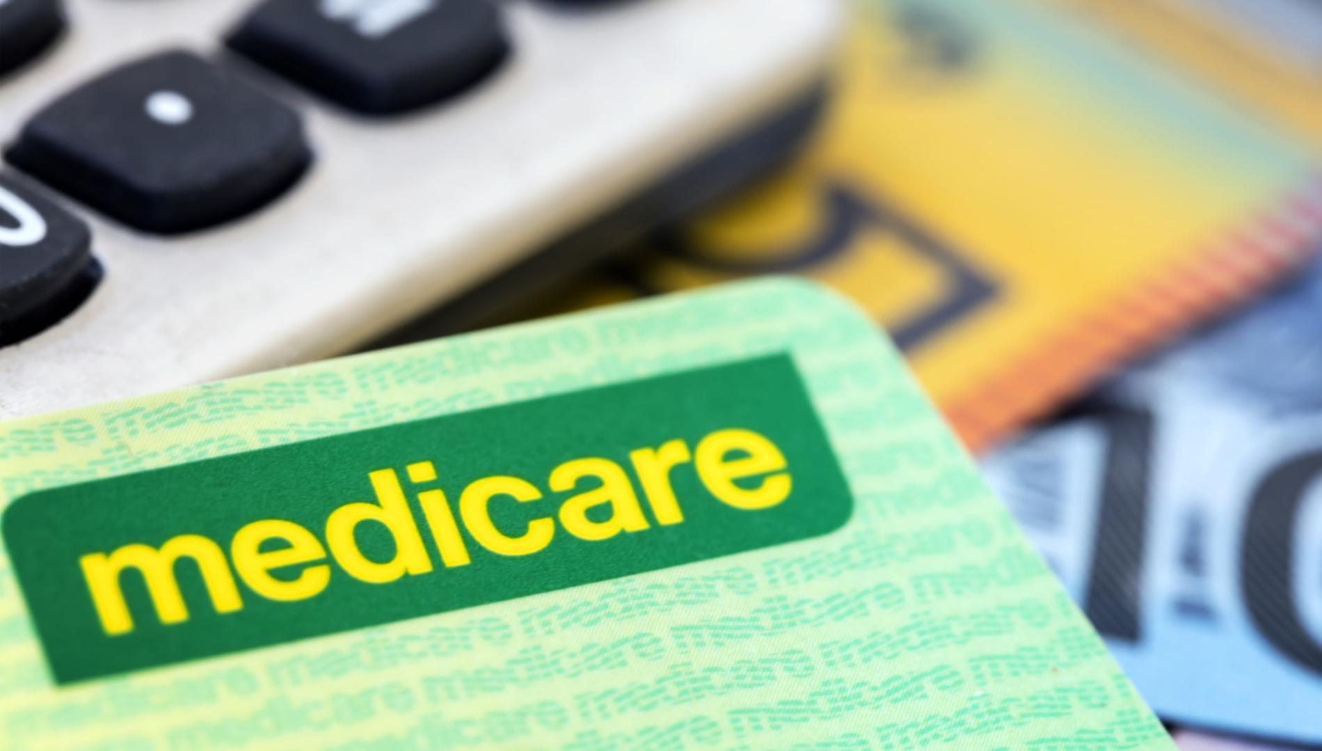 Medicare card sitting on top of cash and a calculator keypad