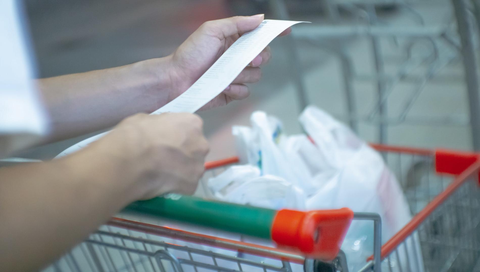 A person with bags of groceries in a trolley, checking the bill