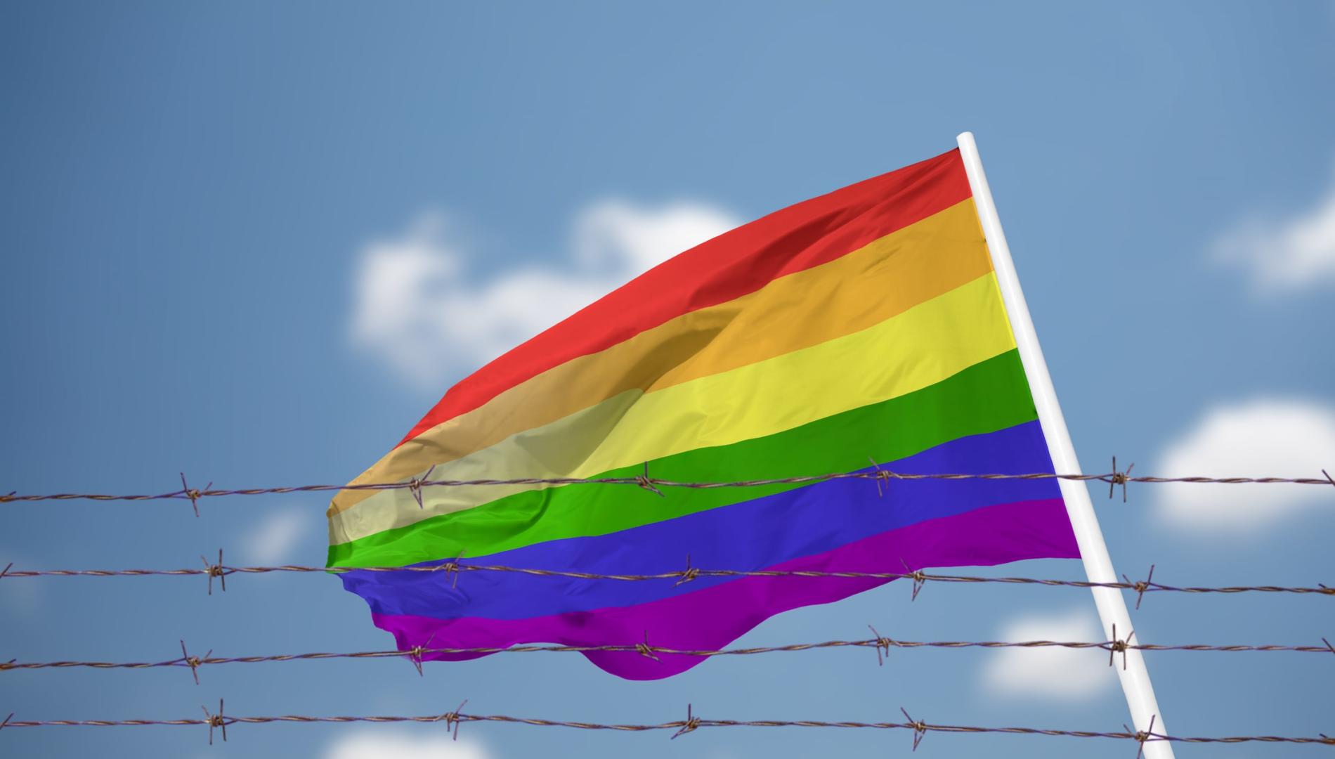 An LGBTQAI+ pride flag waving behind barbed wire