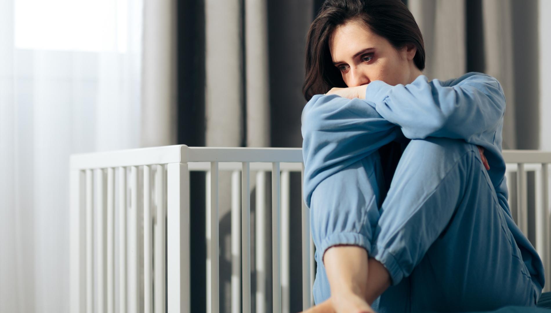 A woman sits next to n empty crib.