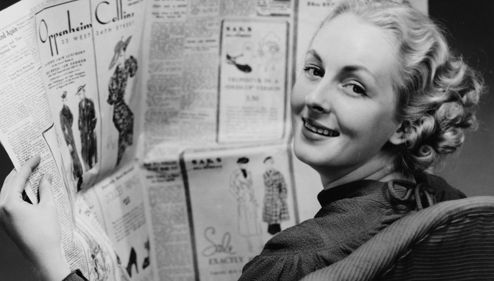 A woman reads a newspaper with a number of large fashion advertisements.