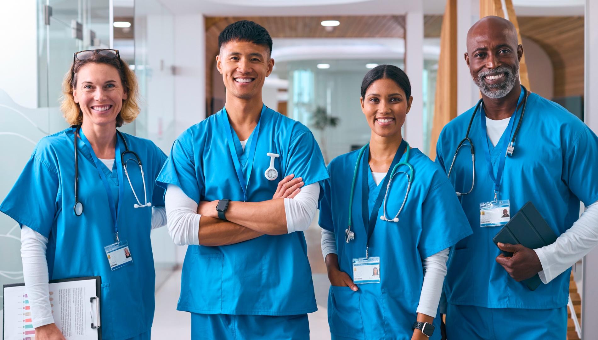 Portrait Of Smiling Multi Cultural Medical Team Wearing Scrubs In Modern Hospital