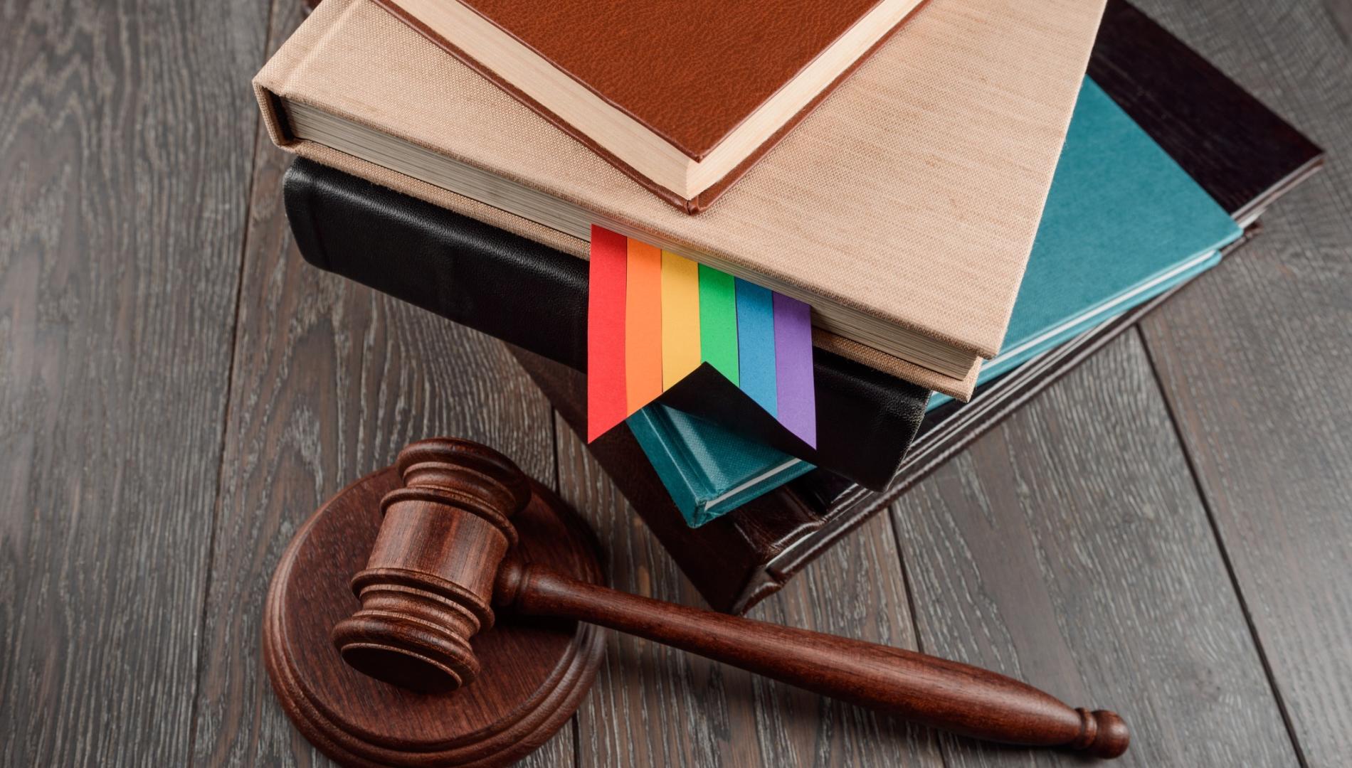 Judge's gavel and books with a gay rainbow bookmark on wood table. LGBT rights, justice and law equality concept.