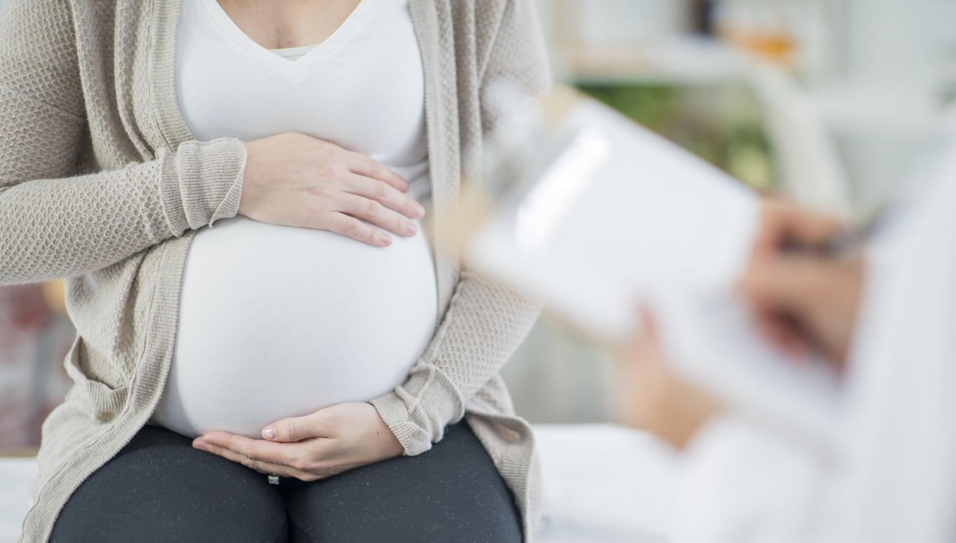 A pregnant woman holds her stomach as a doctor takes notes on a clipboard