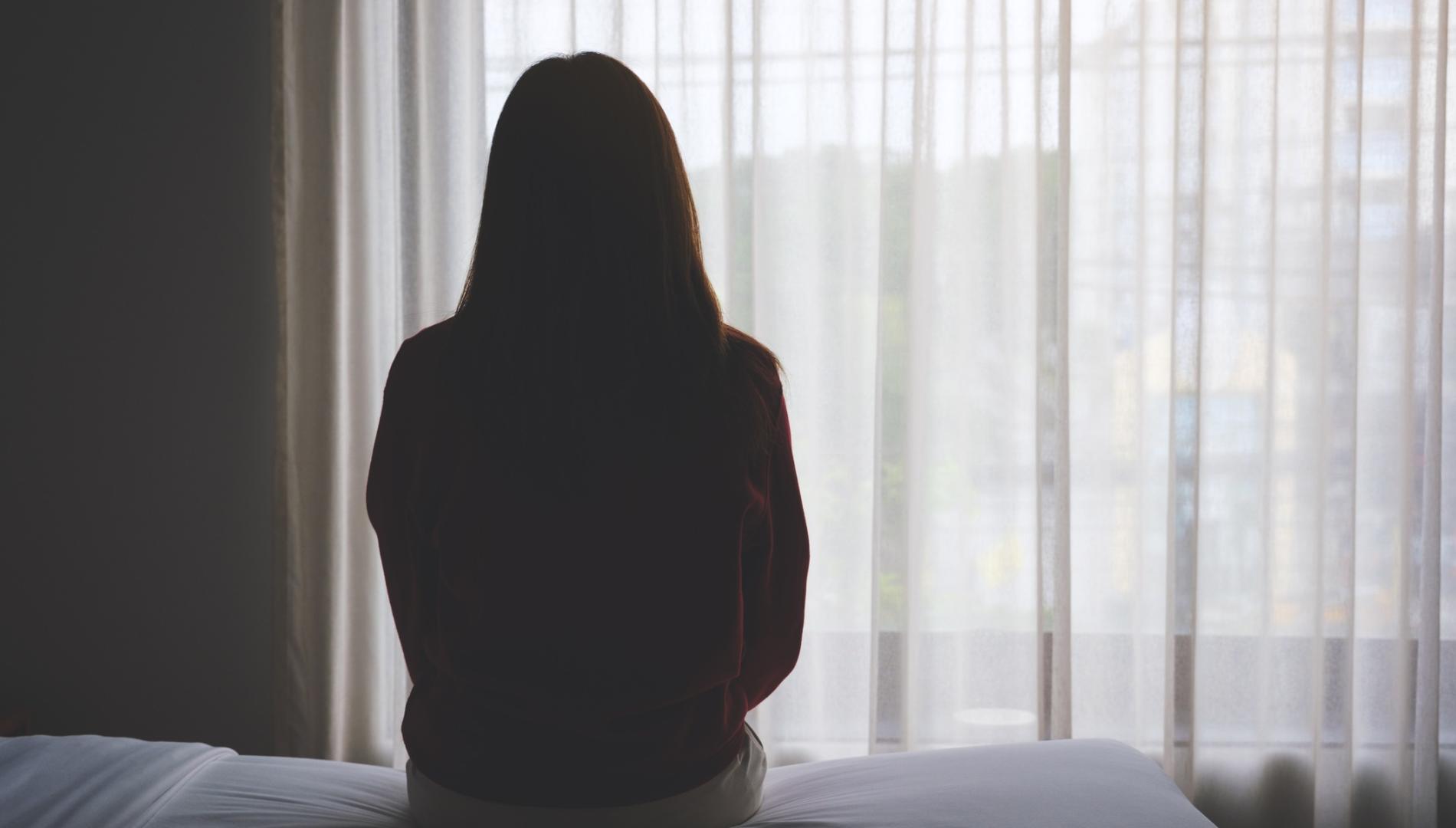 Rear view image of a woman sitting alone on a bed in bedroom