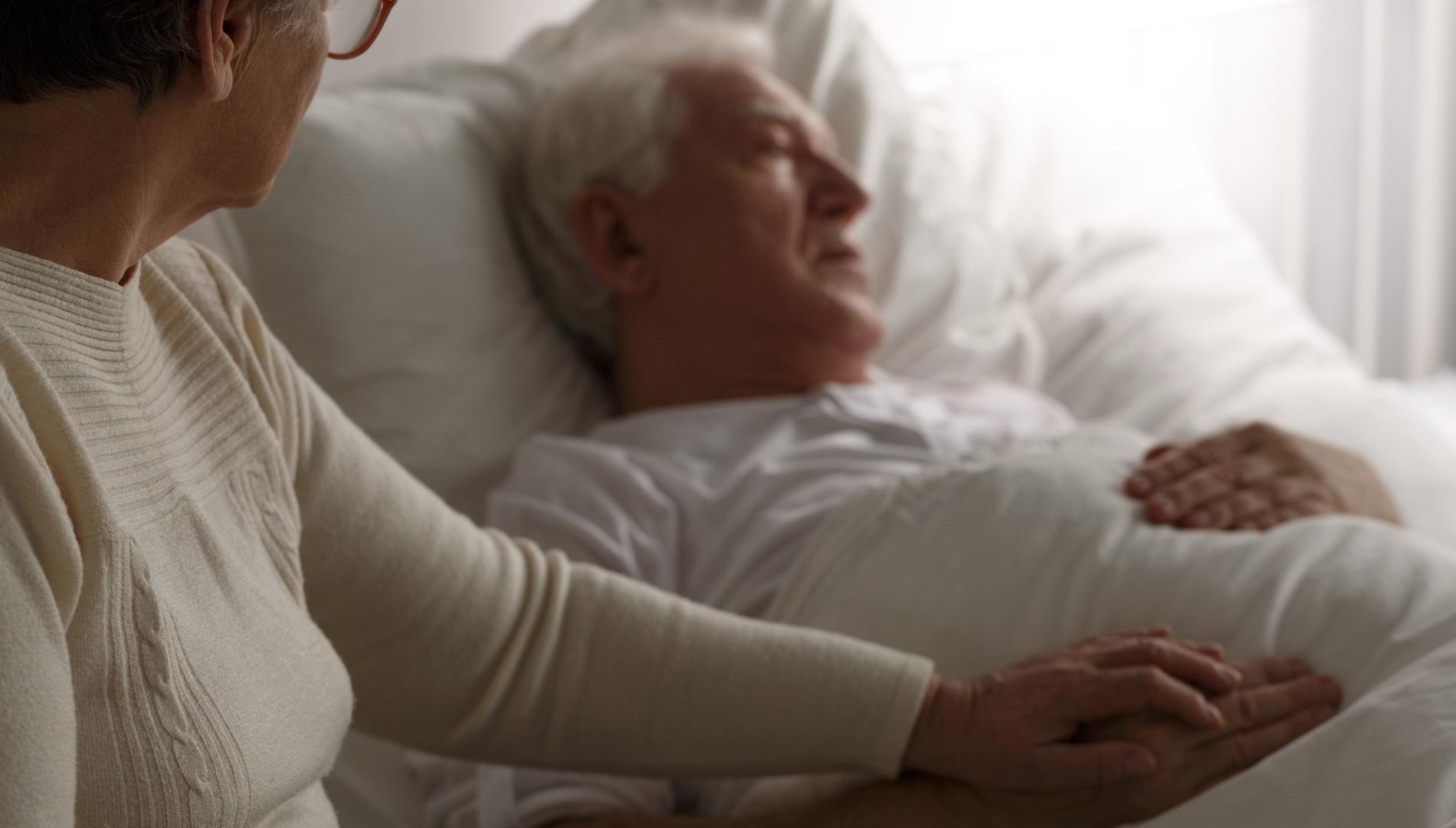 Sad senior man in hospital bed and his wife sitting next to him