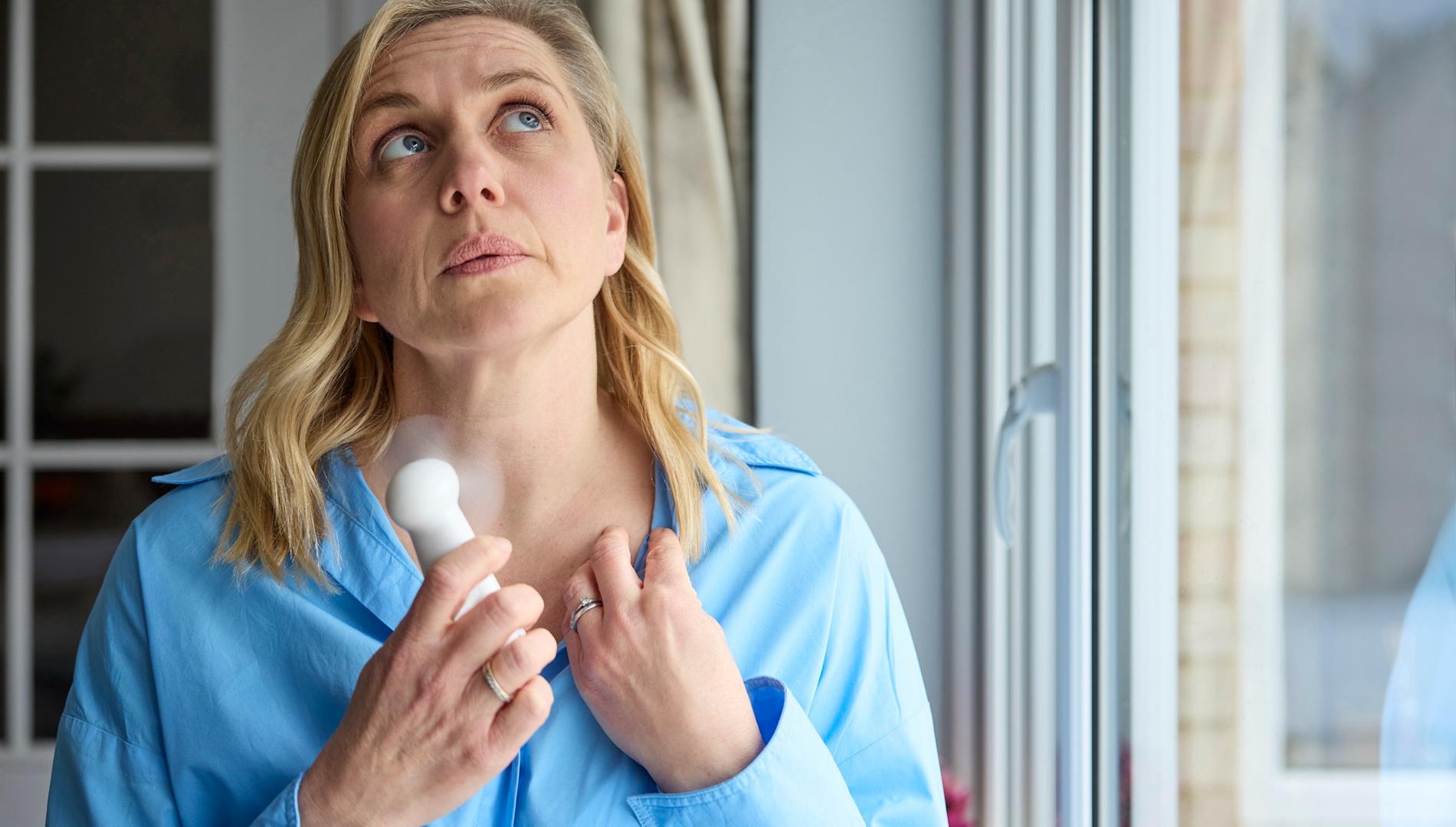 Menopausal mature woman having a hot flush, cooling herself with a handheld electric fan