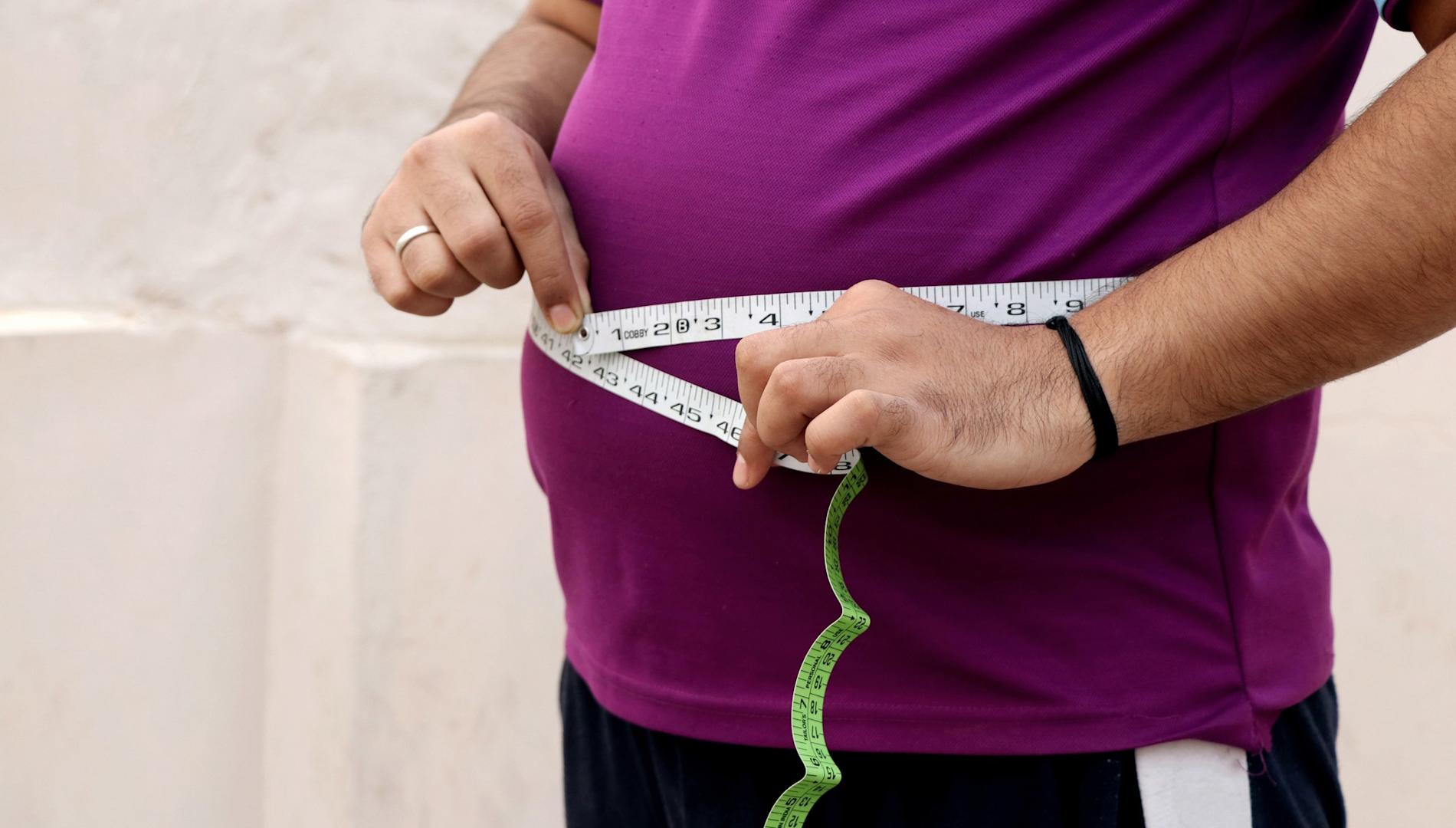 A man measuring his waist with a measuring tape.