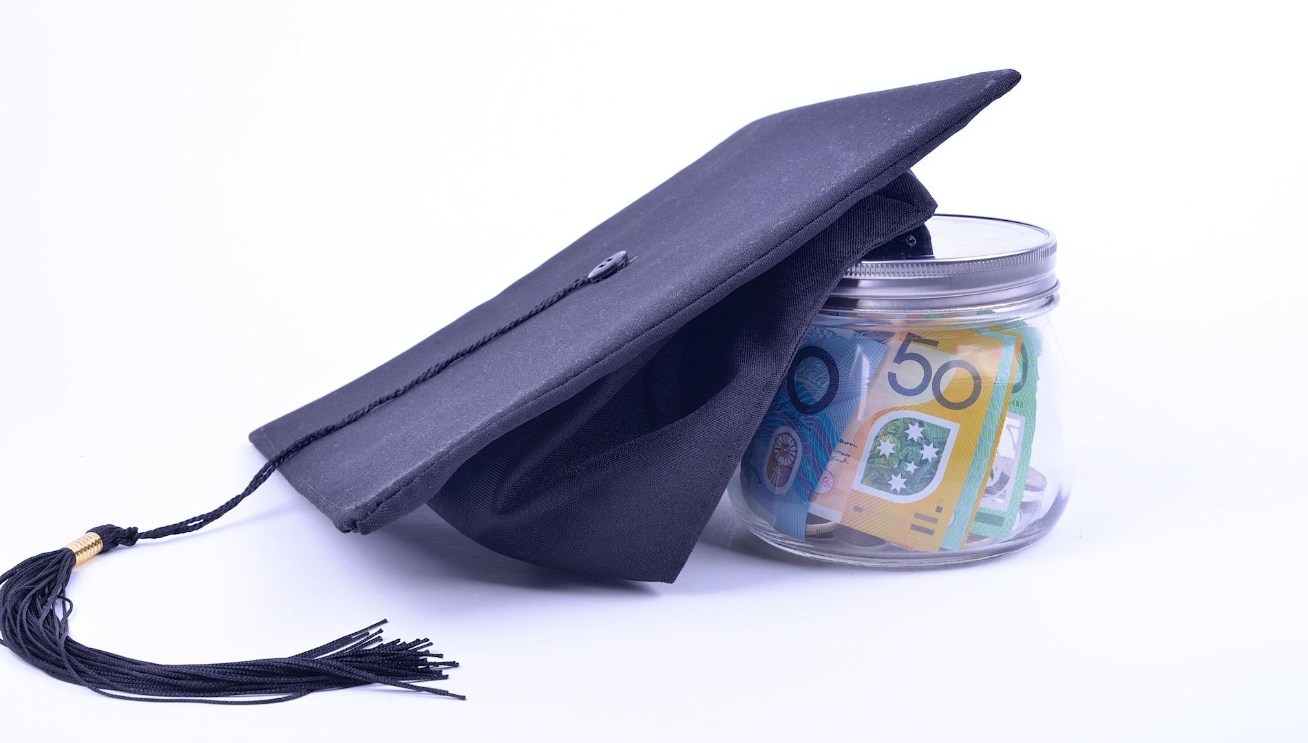 A jar full of Australian money with a mortarboard graduation cap