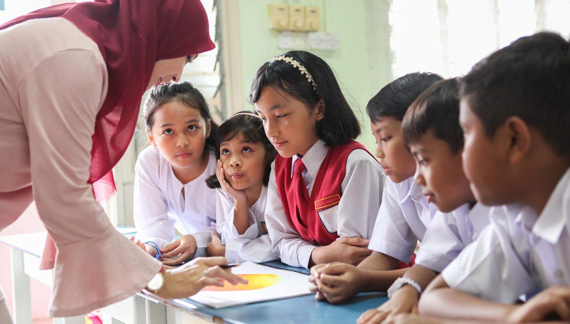 A Malay Muslim female teacher teaching a group of students in a classroom in Malaysia.