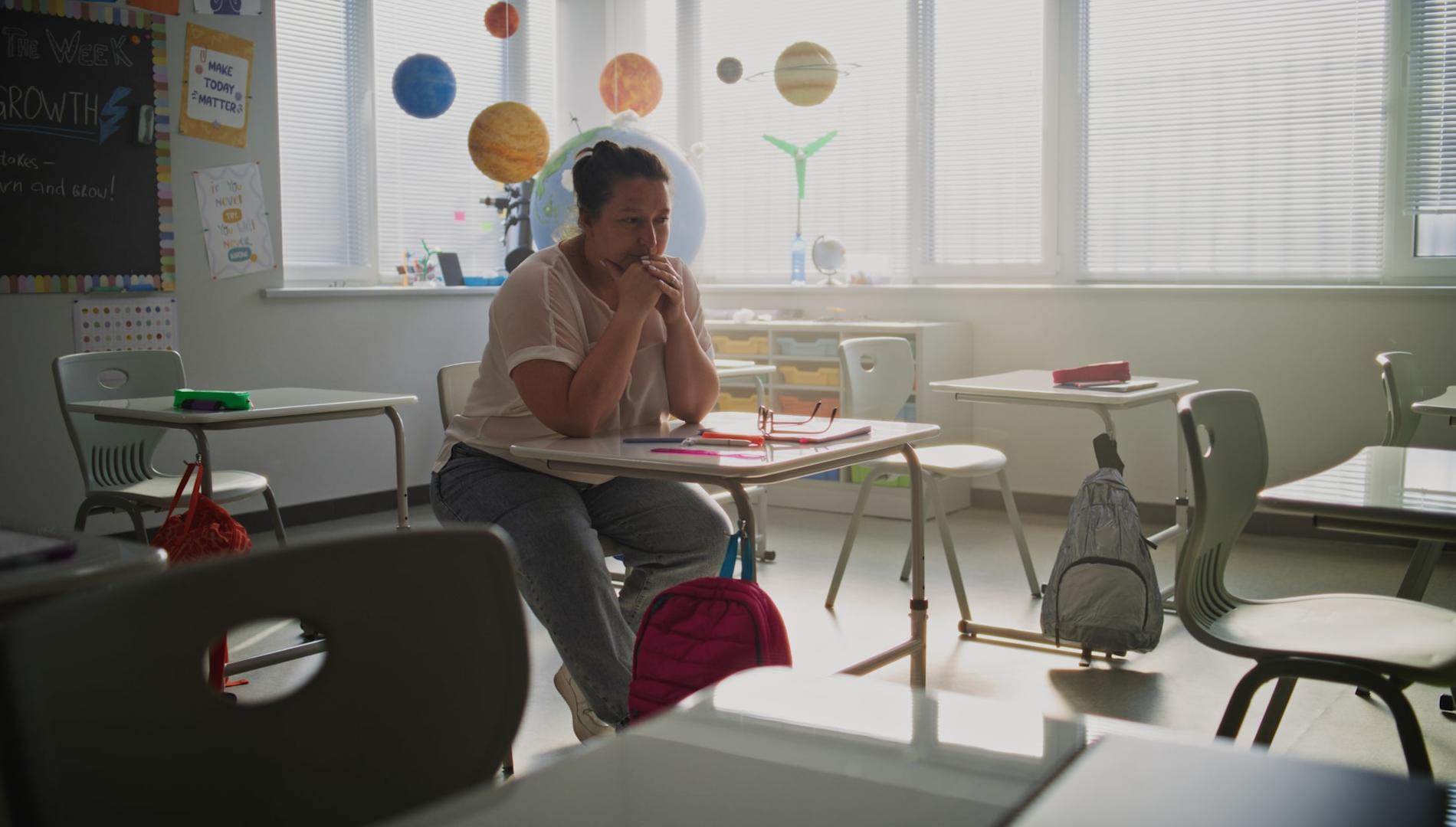 Tired, stressed female teacher sitting in an empty classroom