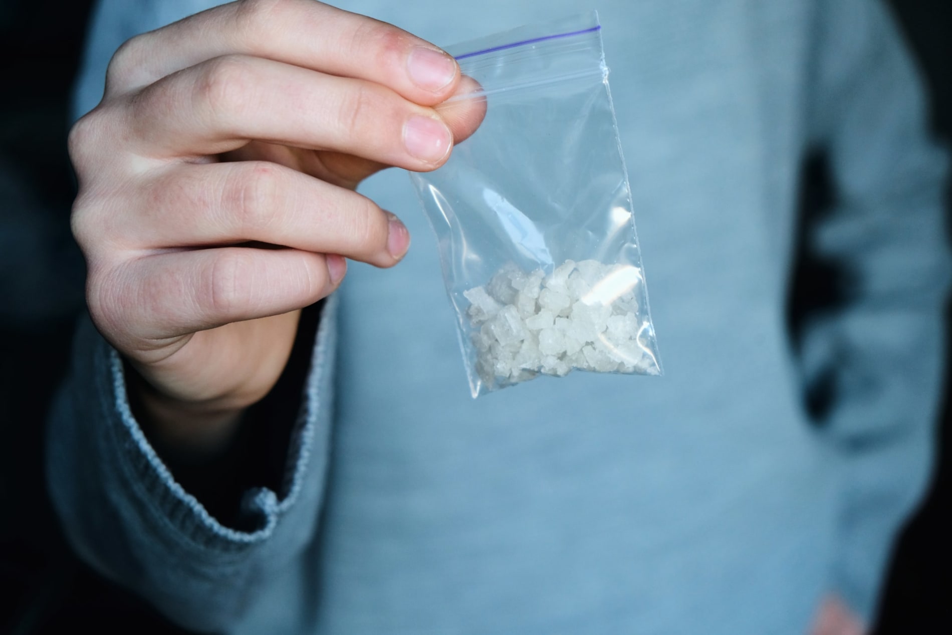 A hand holding a small plastic bag containing methamphetamine crystals