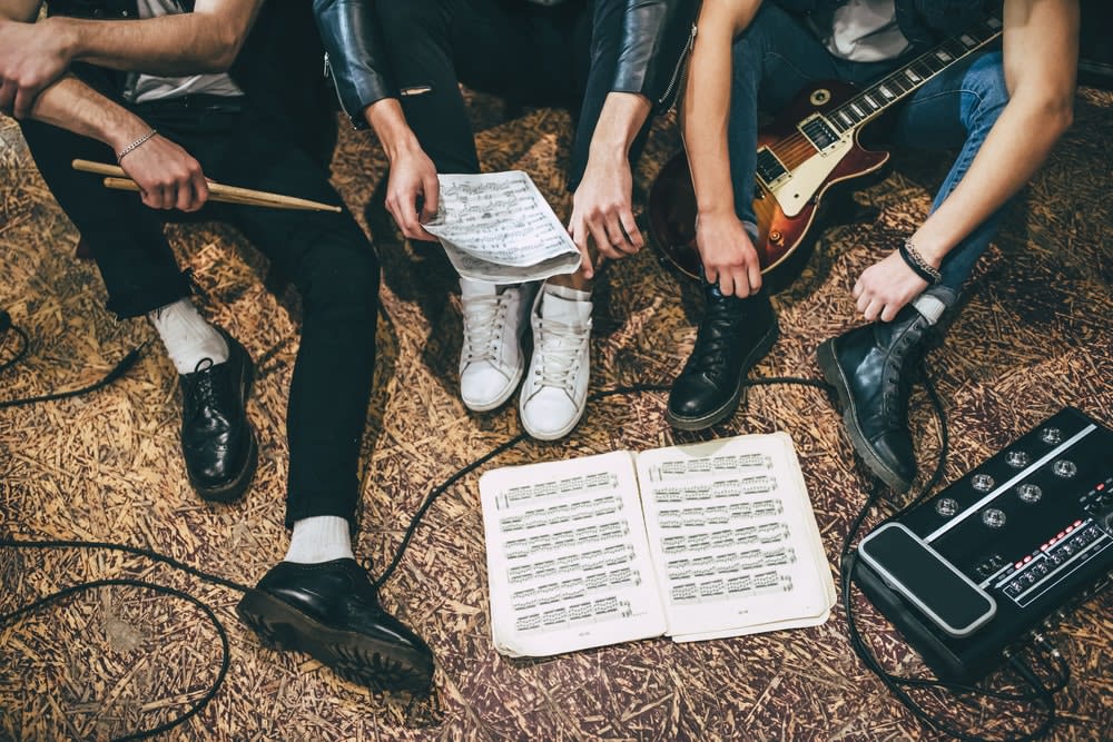 Bandmates, legs and arms visible, sitting with instruments and sheet music on the floor, 