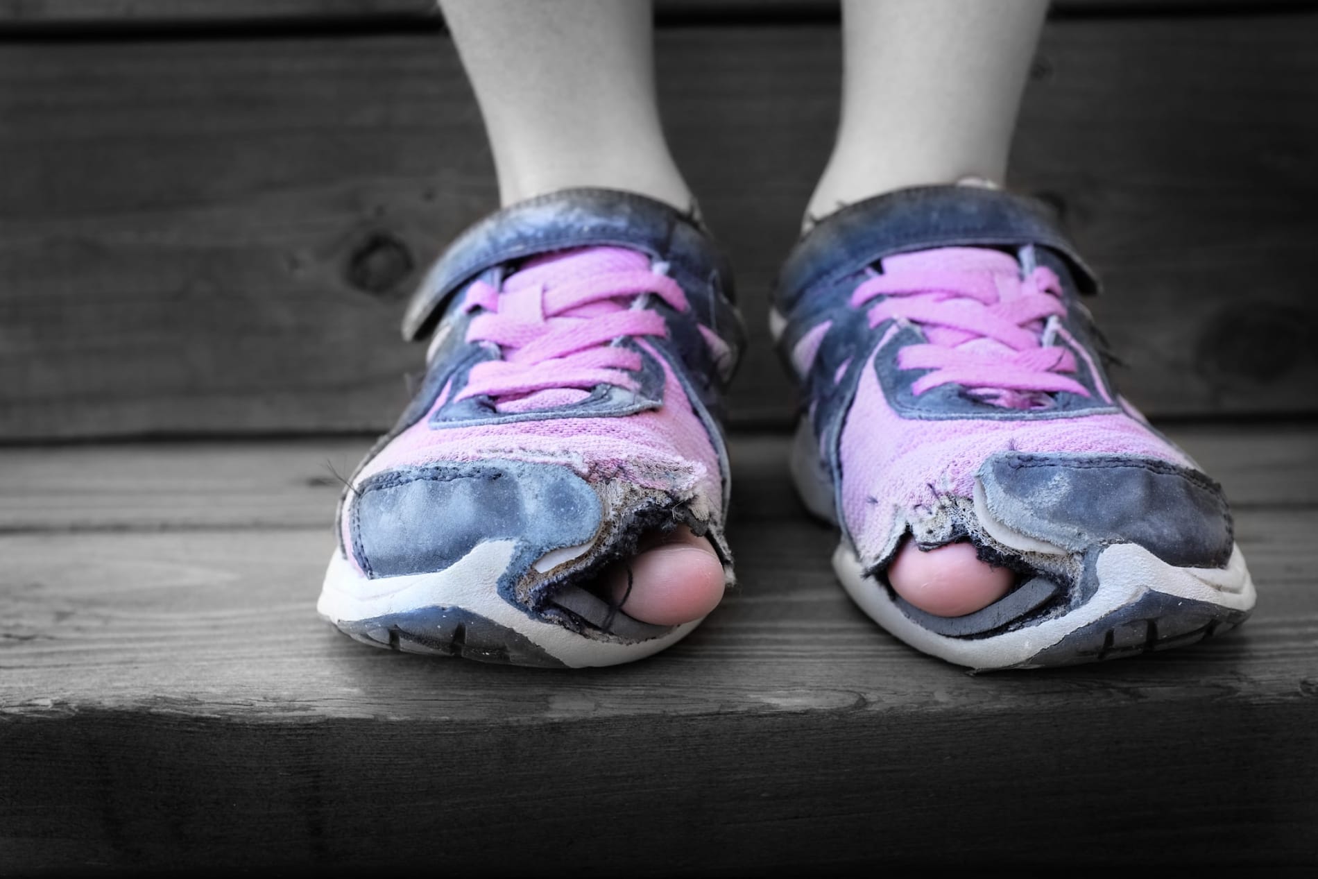 A girl or woman's feet wearing worn out old shoes with holes in the toes