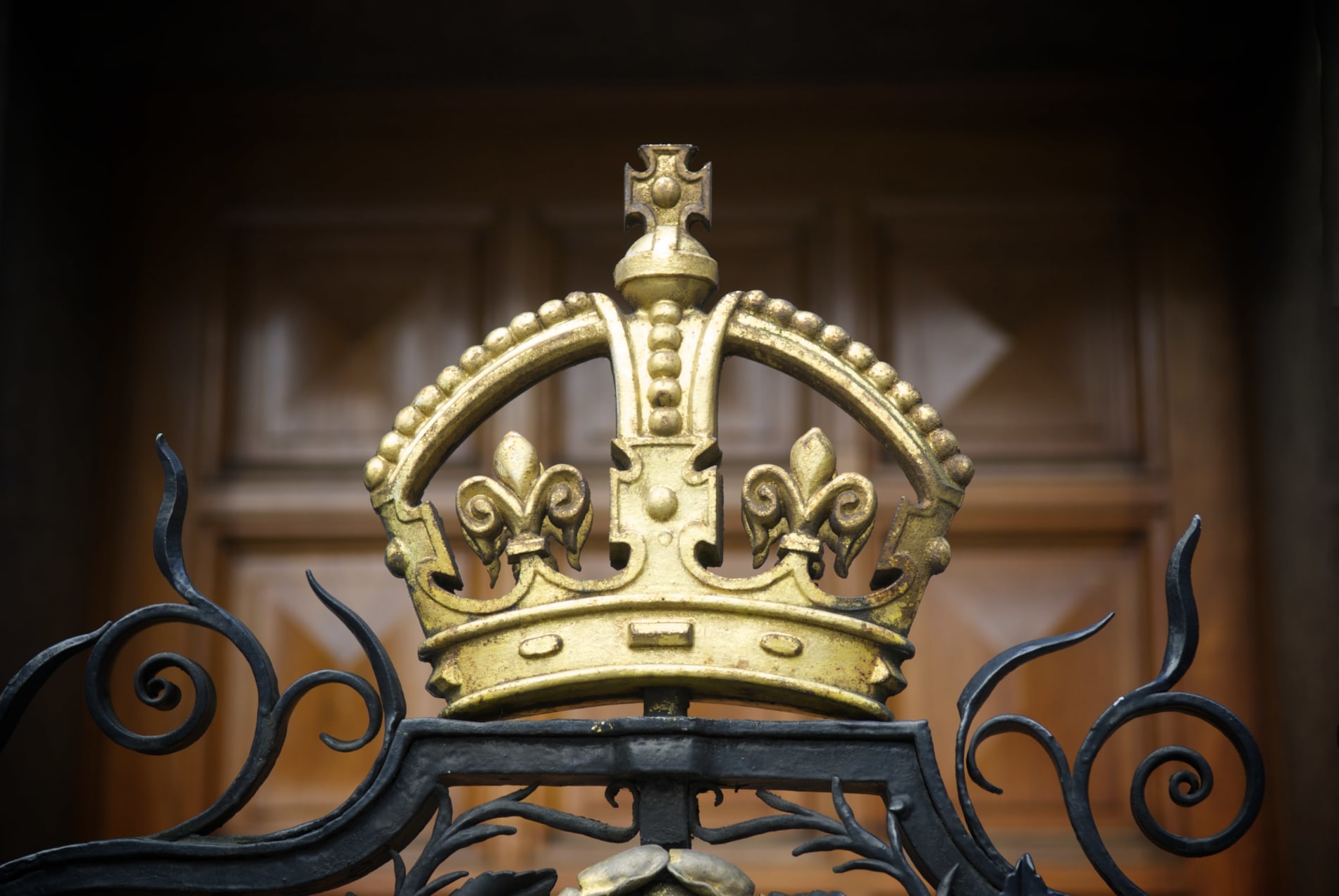 A decorative, gilded crown on a wrought iron fence outside London's National Portrait Gallery with a wood panel door in the background