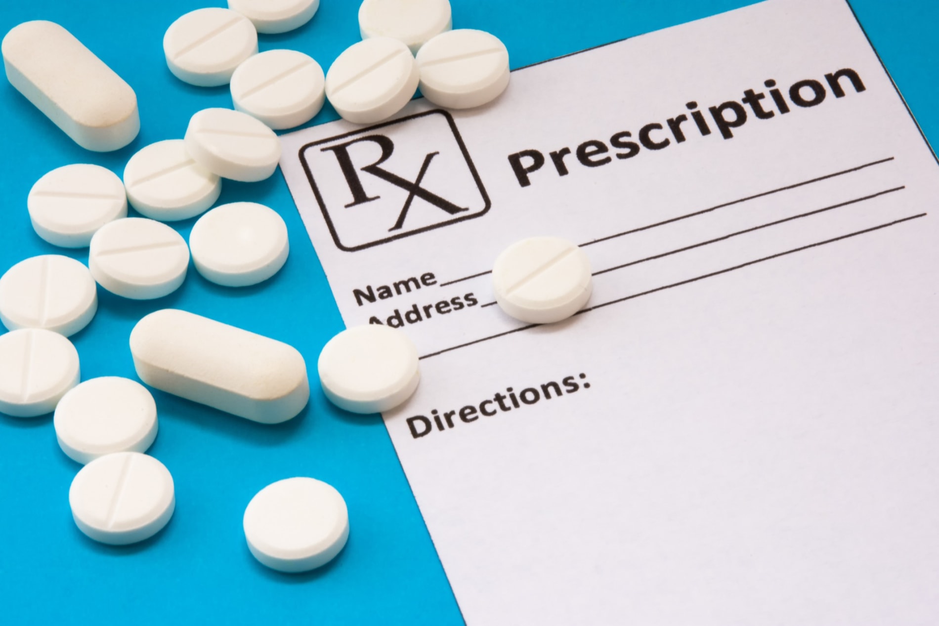  prescription pad is near scattered white pills and tablets on a blue background.