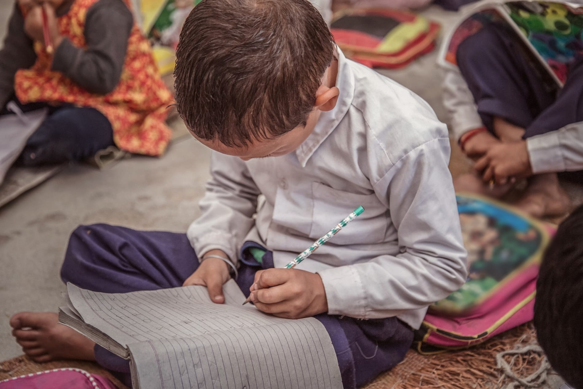 Concentrated Rural school kid studying on floor and writing in the notebook.