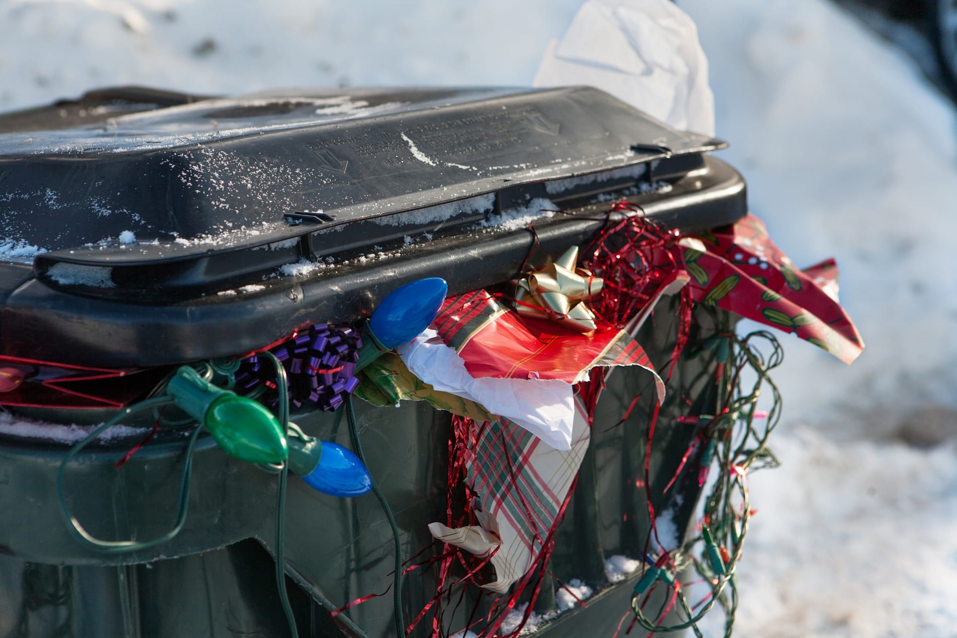 A large plastic rubbish bin overflowing with garbage and discarded Christmas paper lights bows.