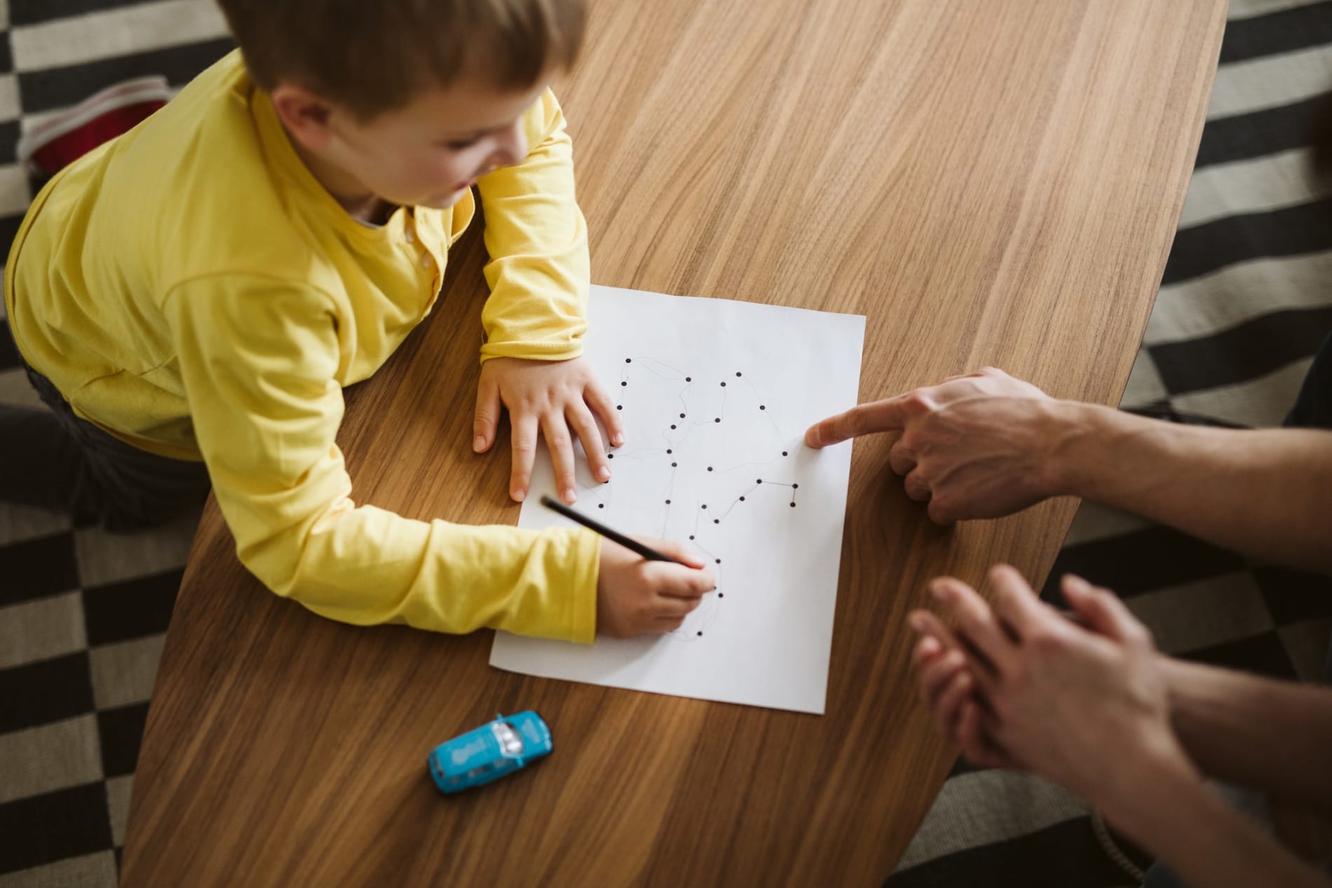 Boy kneeling on the floor and connecting dots on a piece of paper 