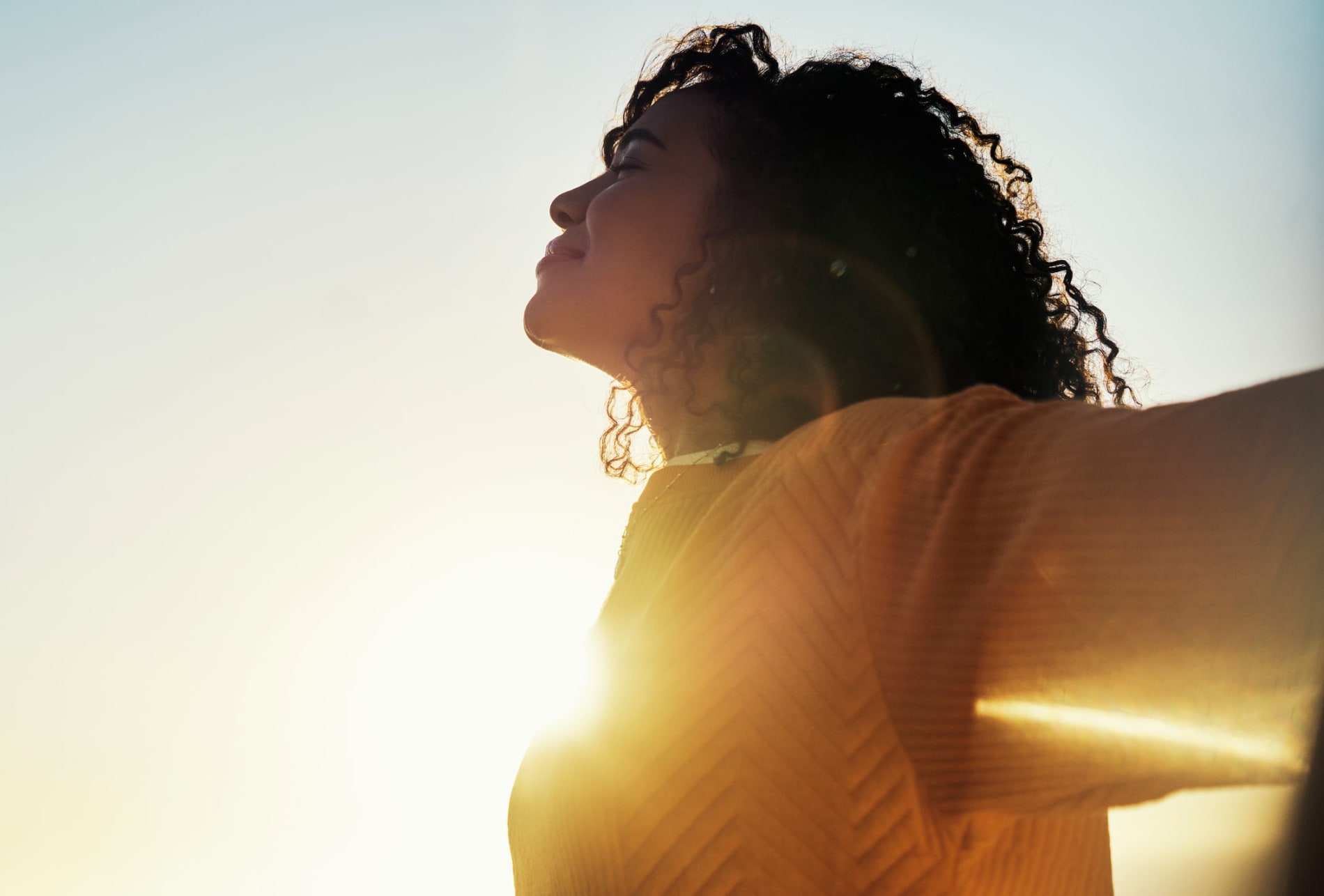 Woman outdoors at sunset or early morning looking relaxed in the sunshine. 