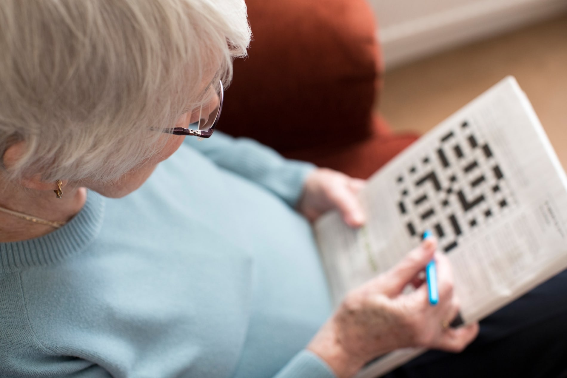 Elderly woman sitting down doing a crossword puzzle.