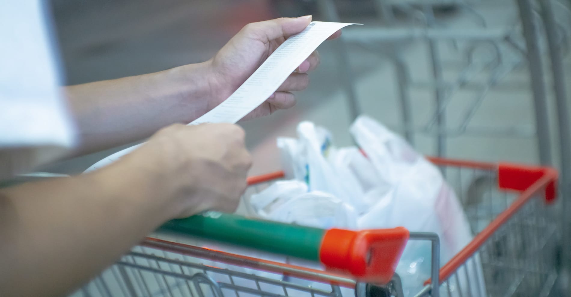 A person with bags of groceries in a trolley, checking the bill