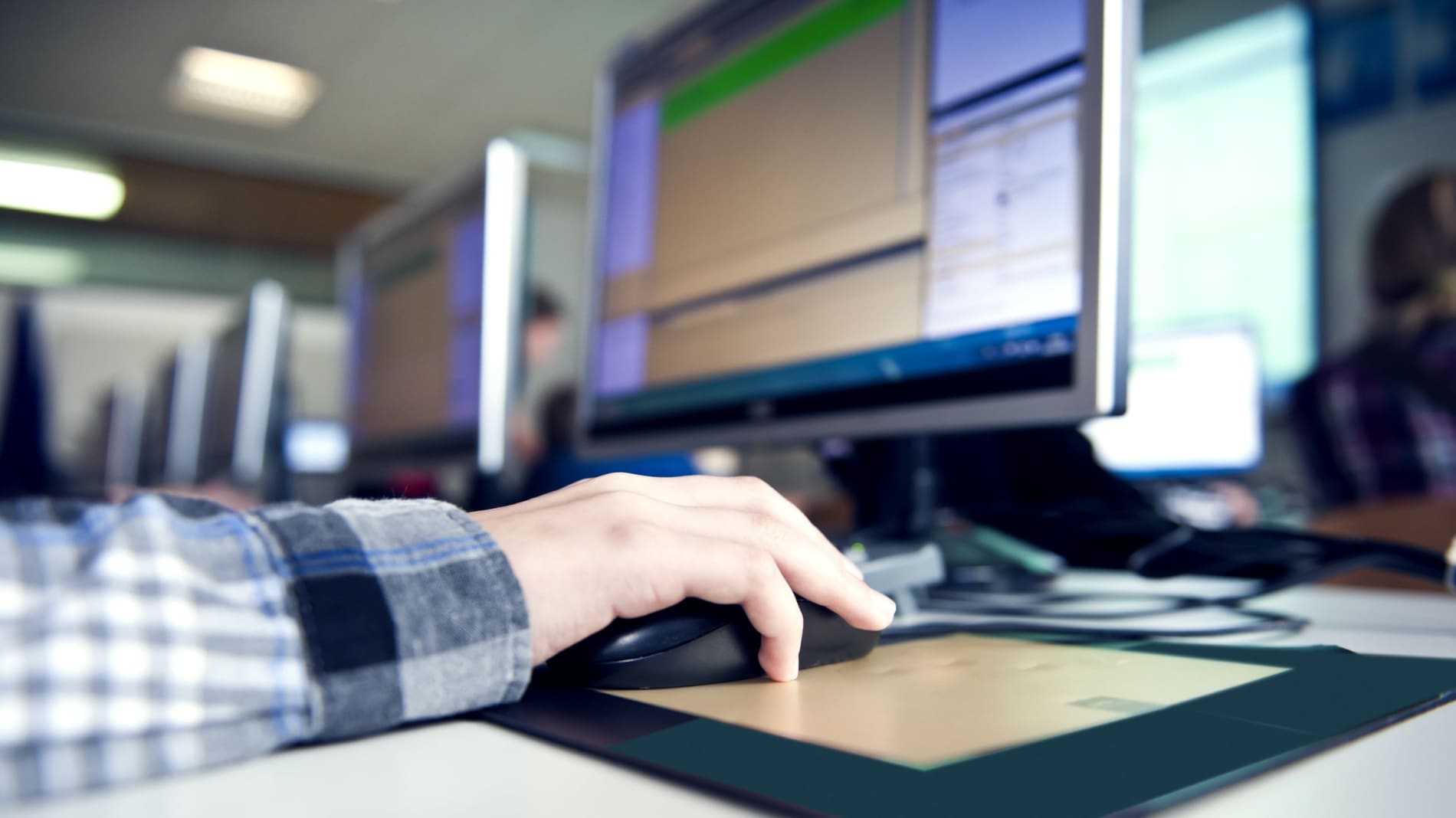 Close-up of a person's hand using a mouse in front of a computer monitor