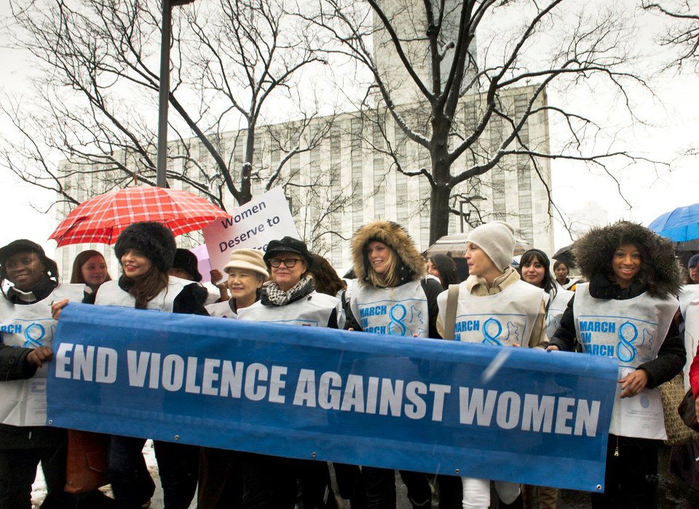 Women march in front of a banner that reads: 'End violence against women'.