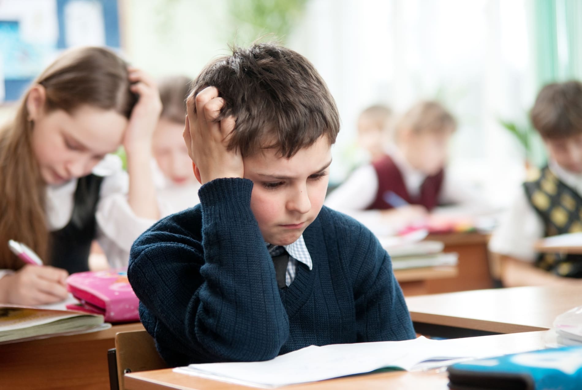 Young boy sitting at a desk doing a test, with his hand resting on his head.