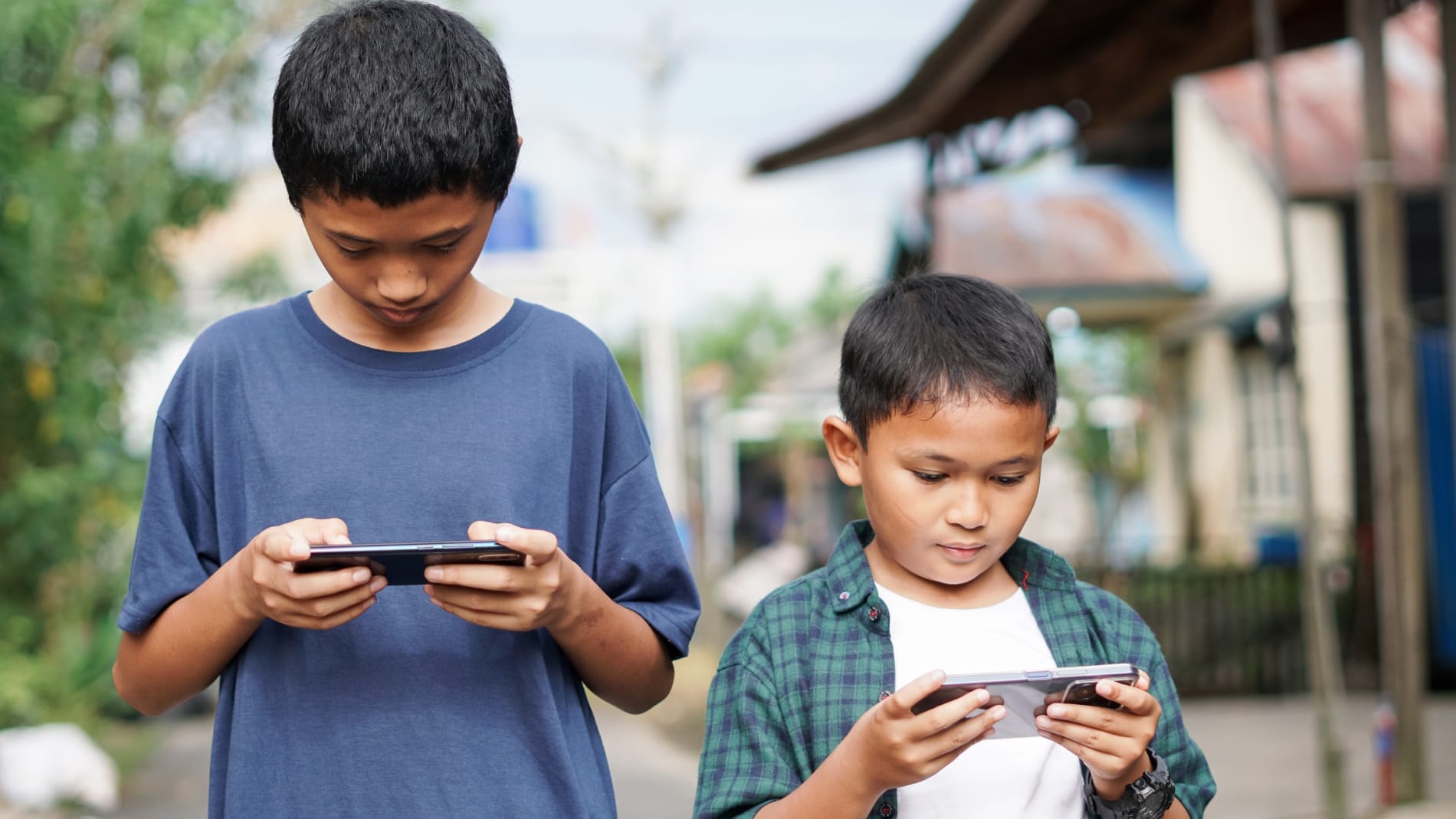 Two young boys outside staring at their mobile phones.