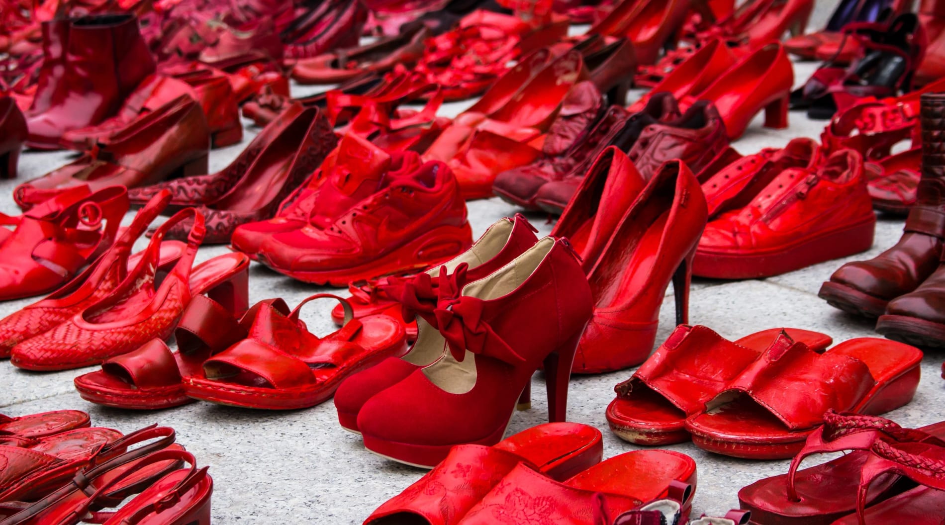 Multiple pairs of red shoes on a concrete floor as a symbol against violence.