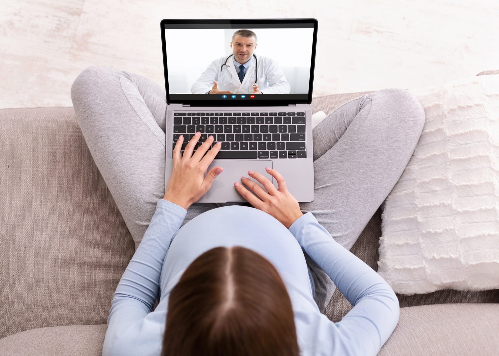 Pregnant women sitting on a couch on a telehealth video appointment with a doctor.