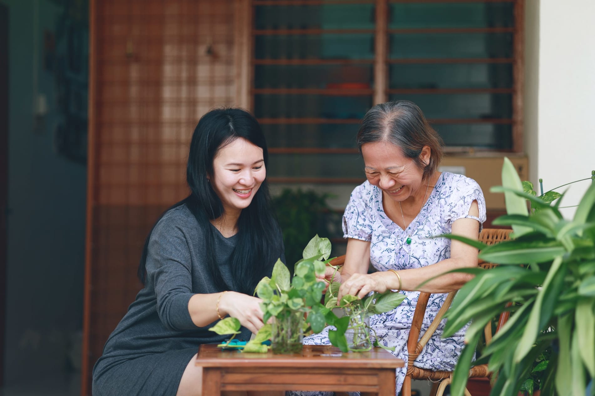 A smiling young Asian woman with her smiling mother, sitting at a table attending to a plant